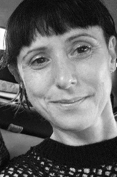 Close-up black and white photo of Lorna Hards with short dark hair smiling slightly.