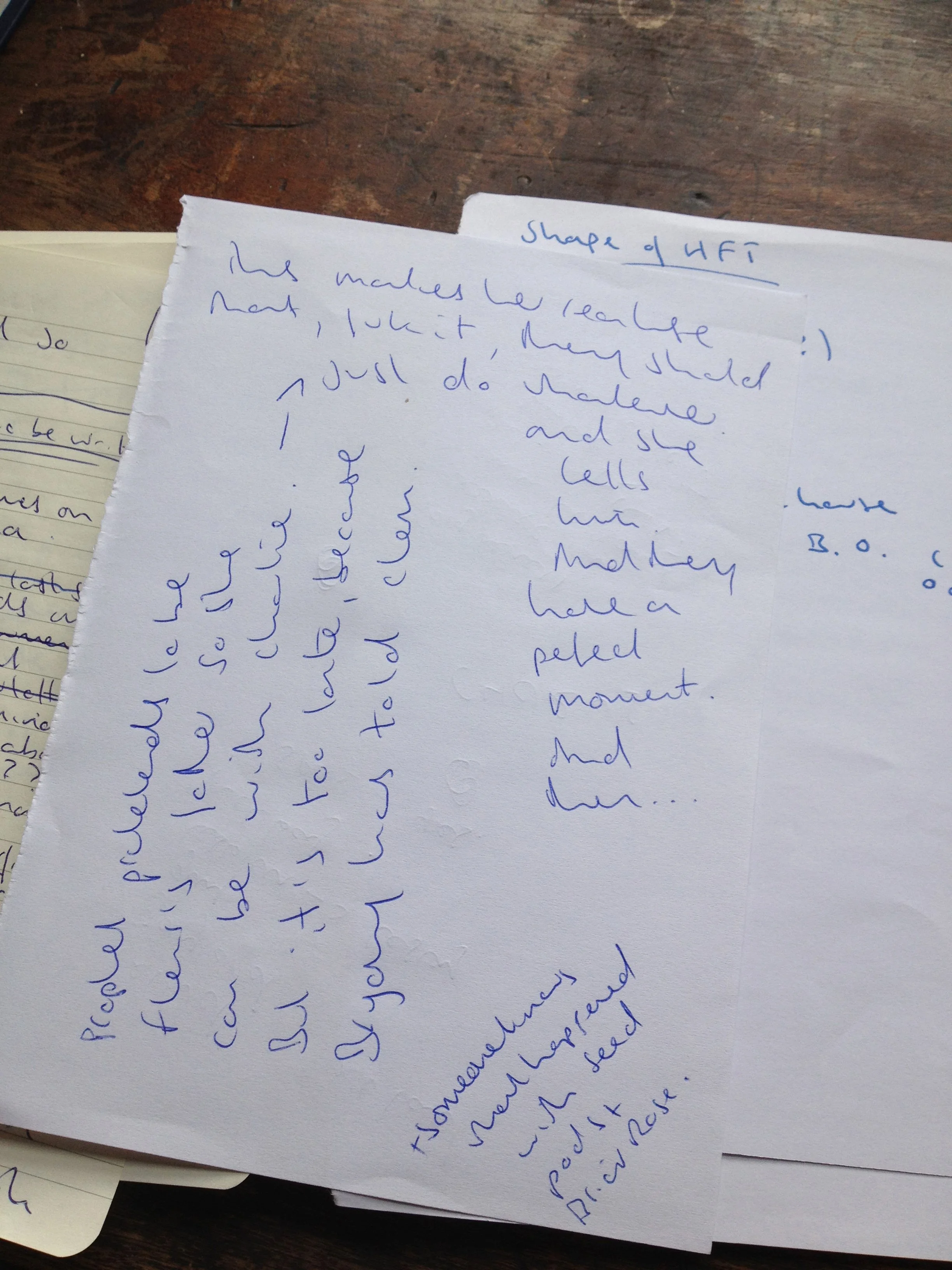 Close-up of handwritten notes on a white paper page titled 'Shape of UFT', with additional notes in blue ink. The paper is placed on a wooden surface, with other notes partially visible underneath.