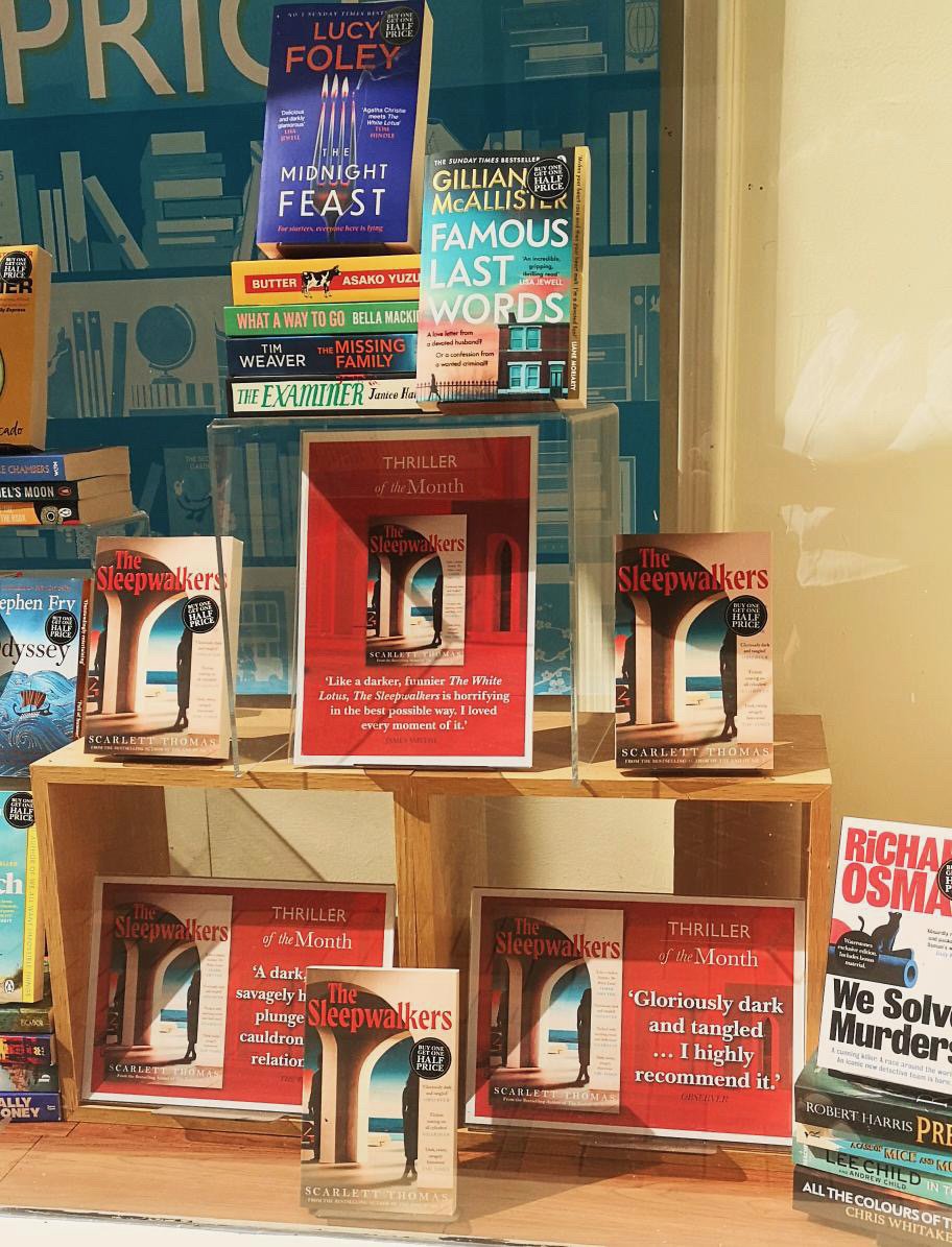 Display of books including 'The Midnight Feast' by Lucy Foley, 'Famous Last Words' by Gillian McAllister, and several copies of 'The Sleepwalkers' by Scarlett Thomas, along with promotional signs.