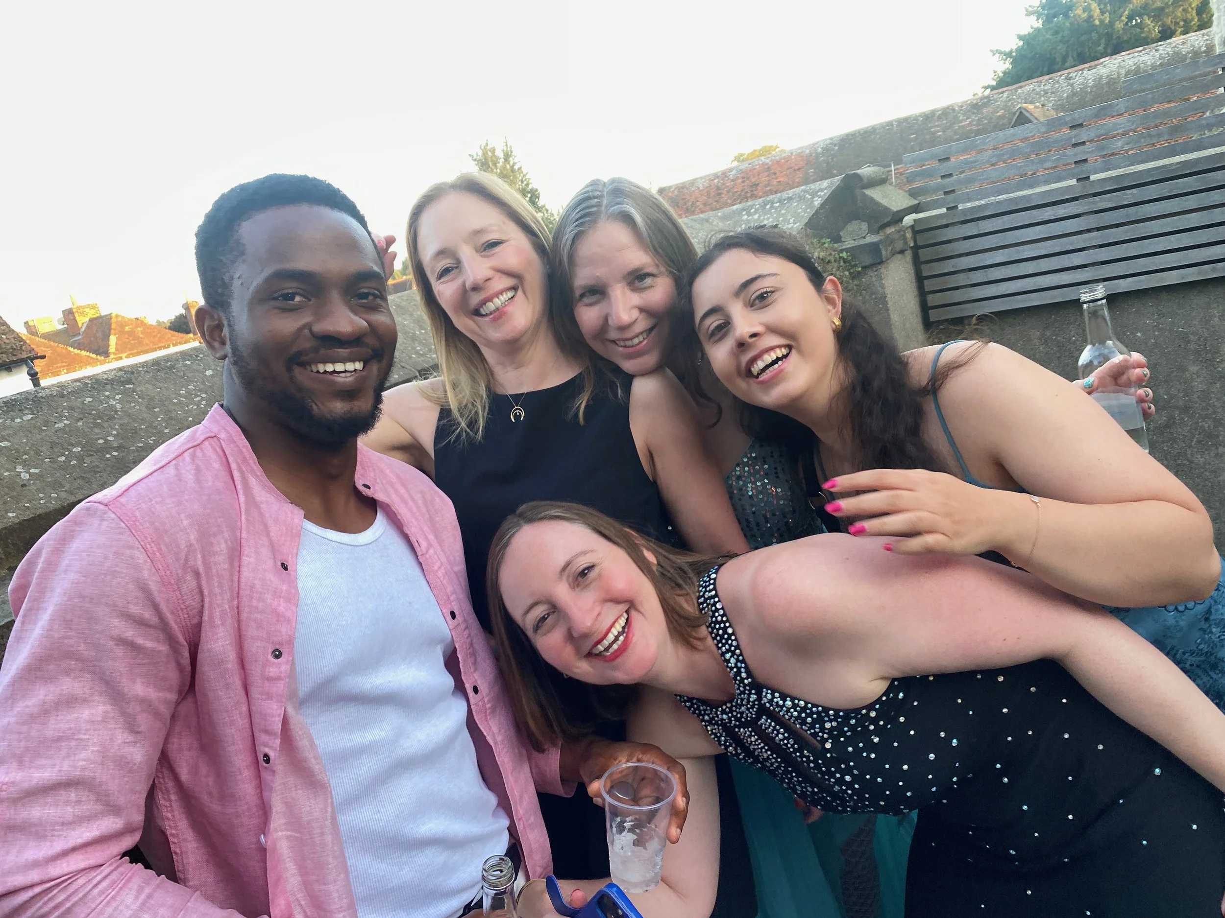 Group of five friends smiling and having a good time outdoors, some holding drinks, in a residential area during evening.