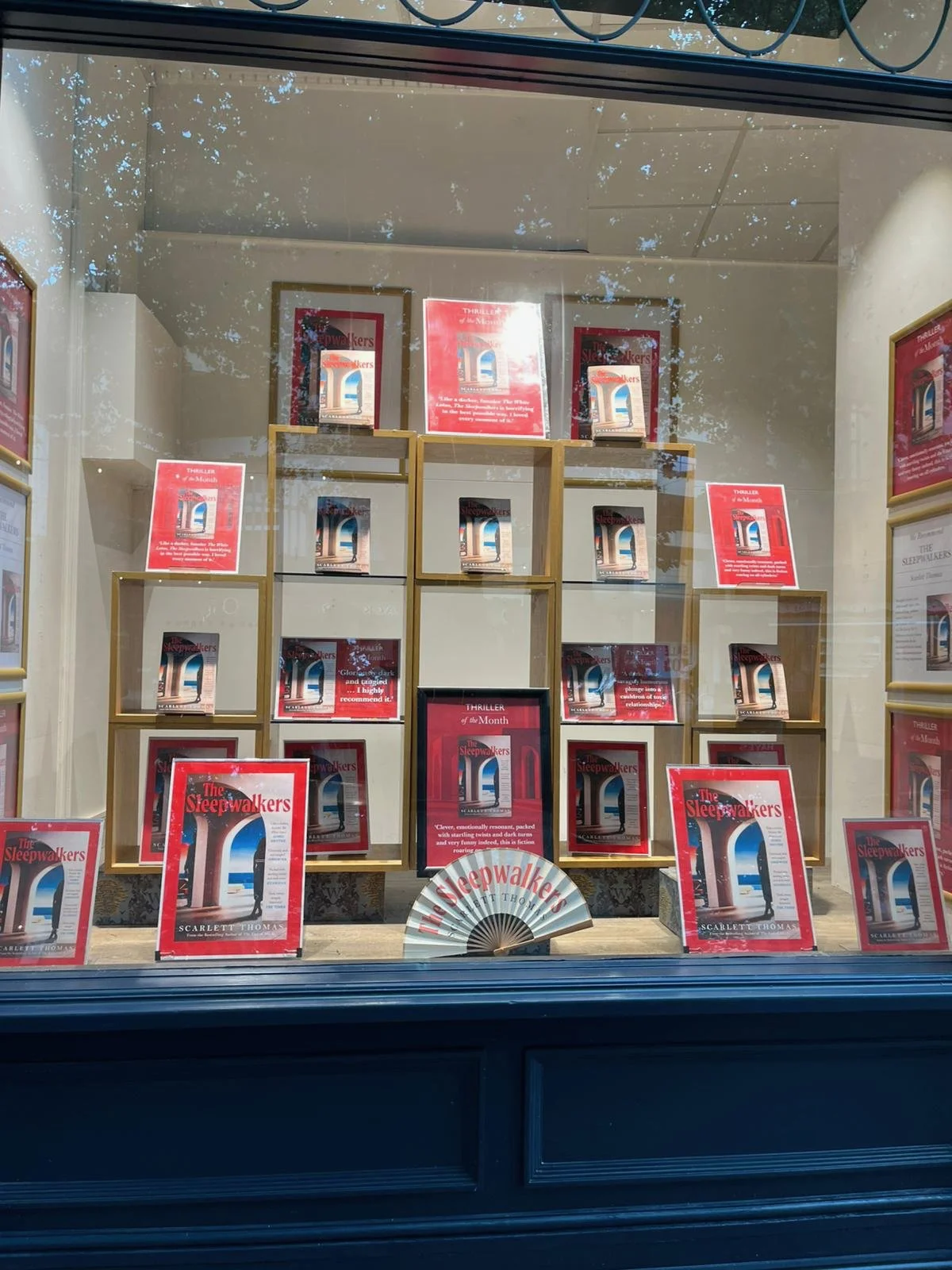 Book display window featuring multiple copies of "The Sleepwalkers" by Scarlett Thomas, arranged on gold-colored shelves with promotional posters and signage.