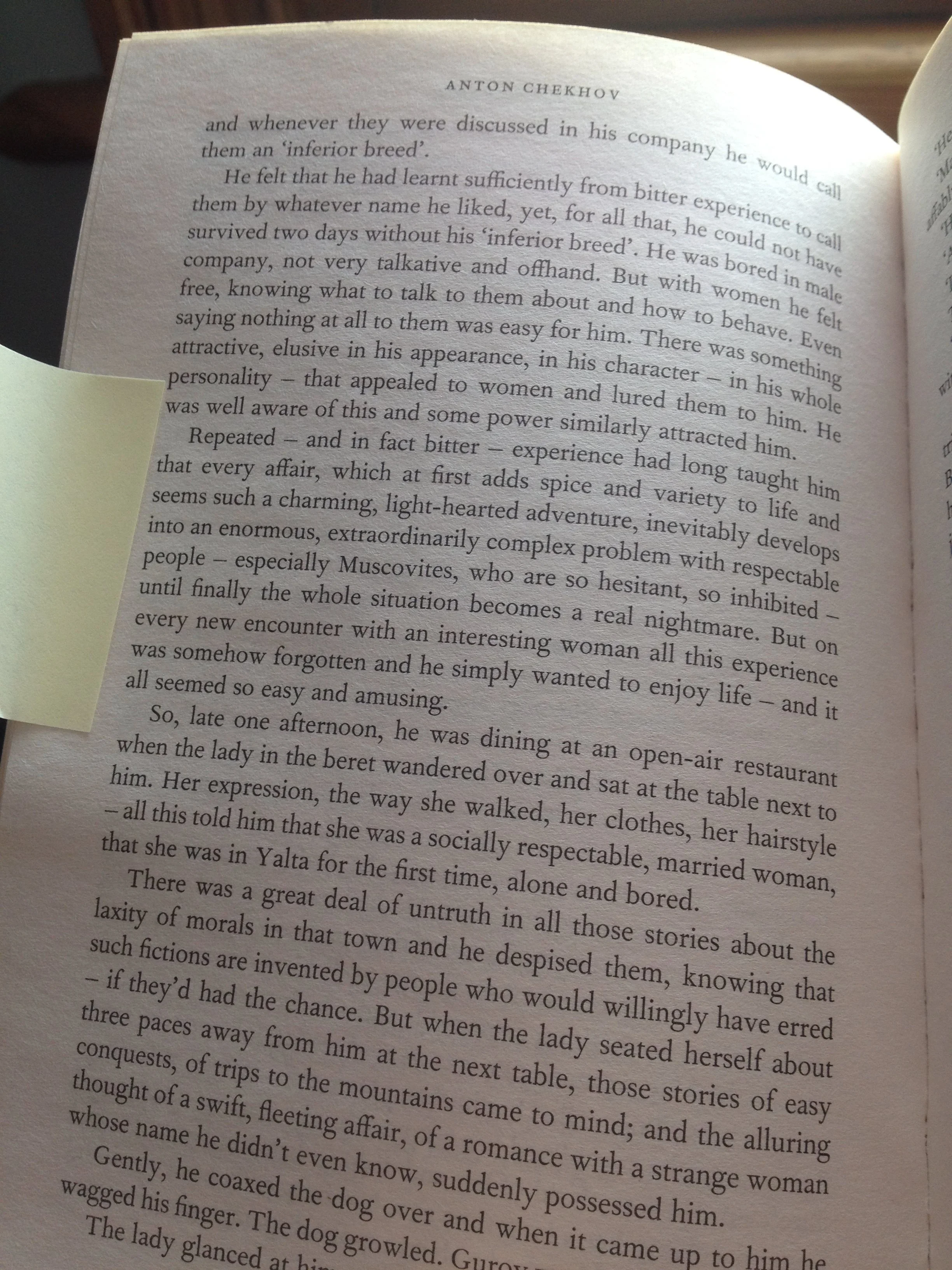 Open book with a sticky note on the left page, showing text from a novel by Anton Chekhov, partially visible with the page slightly curled at the top right.