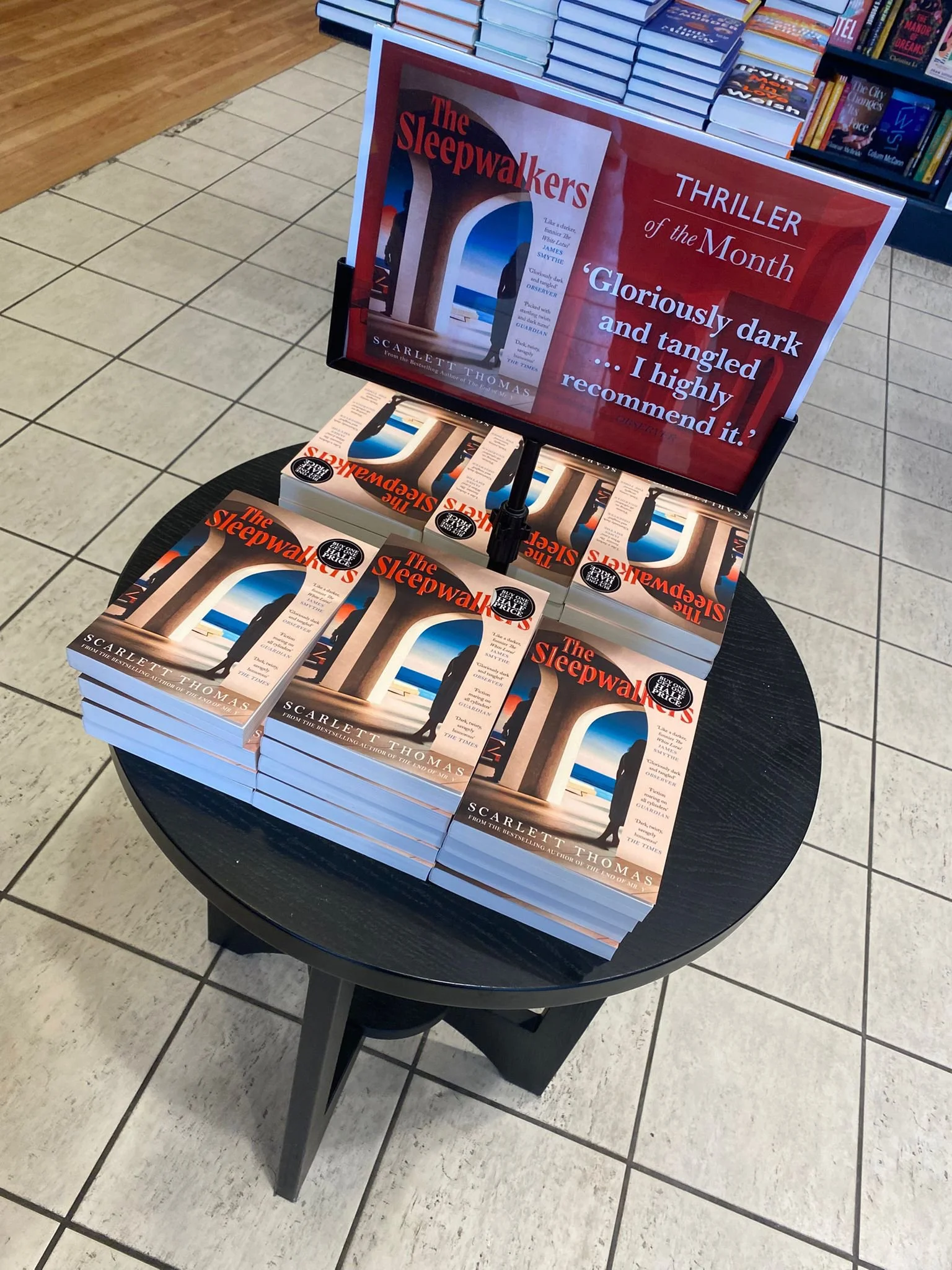 Display table of multiple copies of the book 'The Sleepwalkers' by Scarlett Thomas at a bookstore, with a sign promoting the thriller of the month.