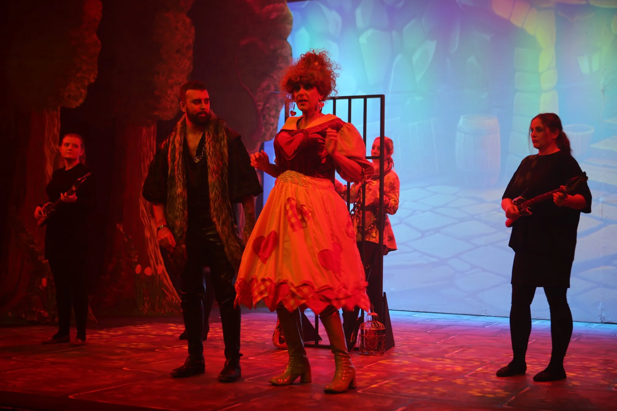 Actors in costume on stage during a theatrical performance with colorful background and props.