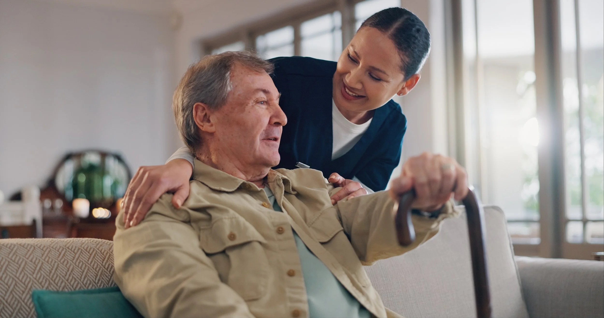 A young woman helps an elderly man in a wheelchair while they share a joyful moment indoors.