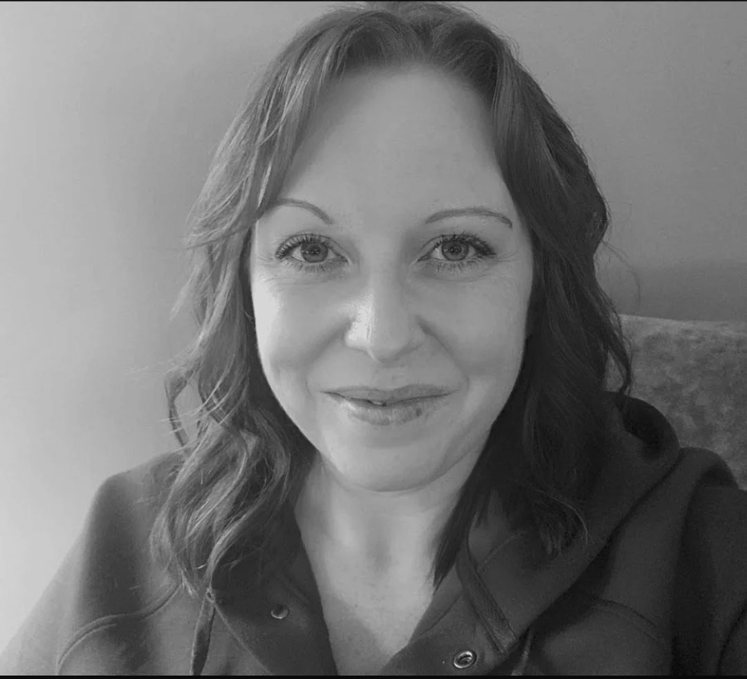 Black and white close-up portrait of a woman with wavy hair, smiling softly, wearing a dark hoodie.