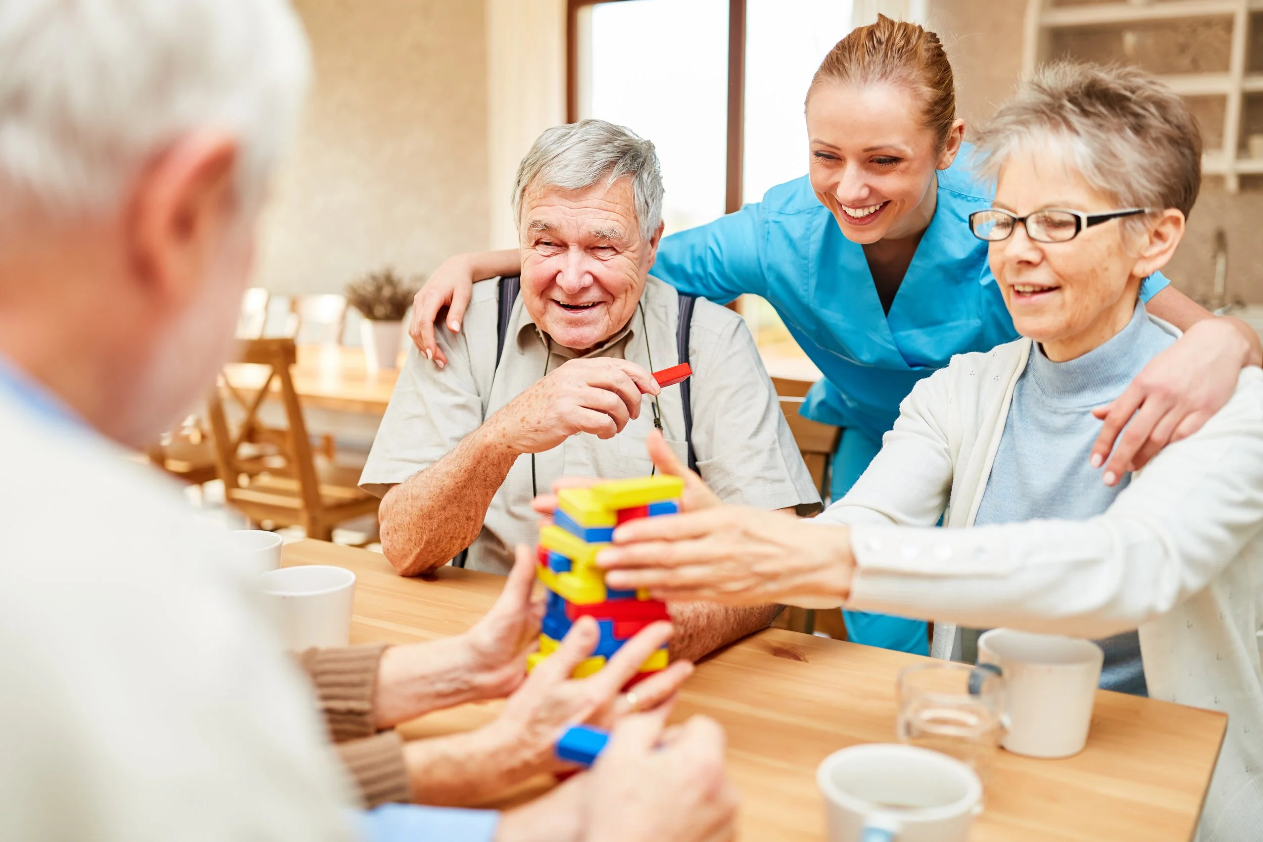 Nursing home residents playing a game of Jenga with a young nurse assisting.