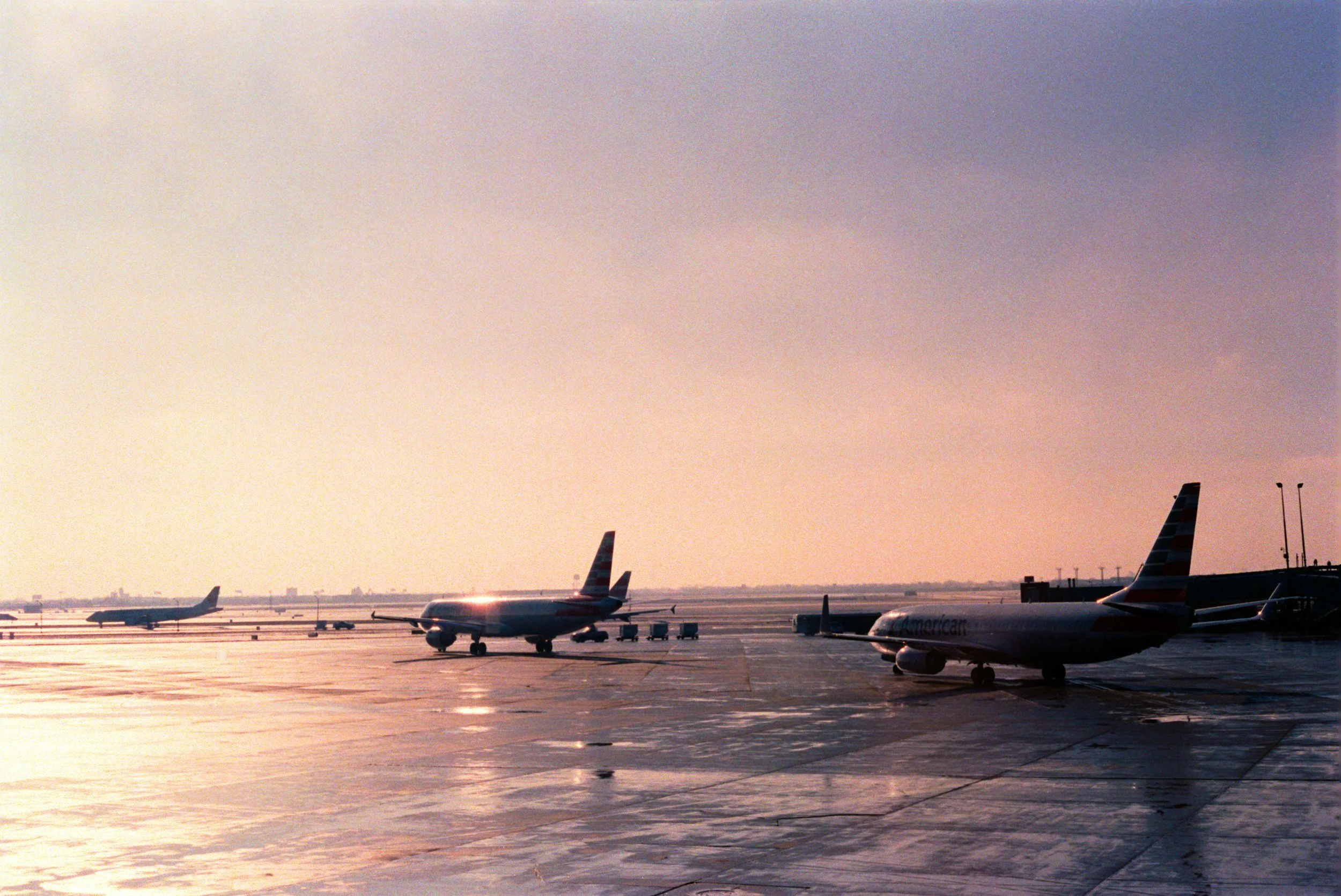 Several airplanes parked on the tarmac at an airport during sunset, with a colorful sky and a flat horizon in the background.
