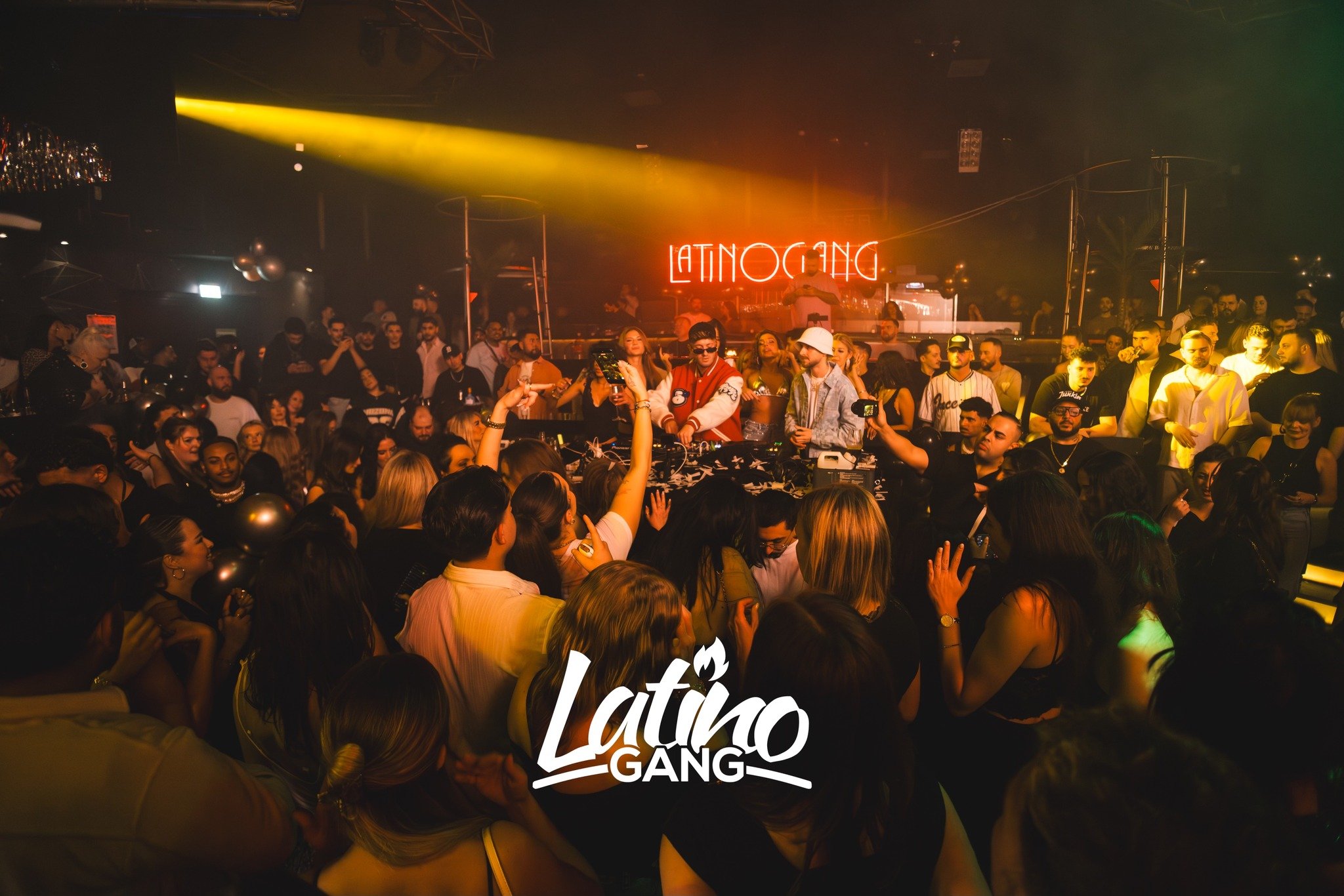 Menschen tanzen und feiern in einem Club mit Neon-Schriftzug im Hintergrund, der 'LATINO GANG' zeigt.