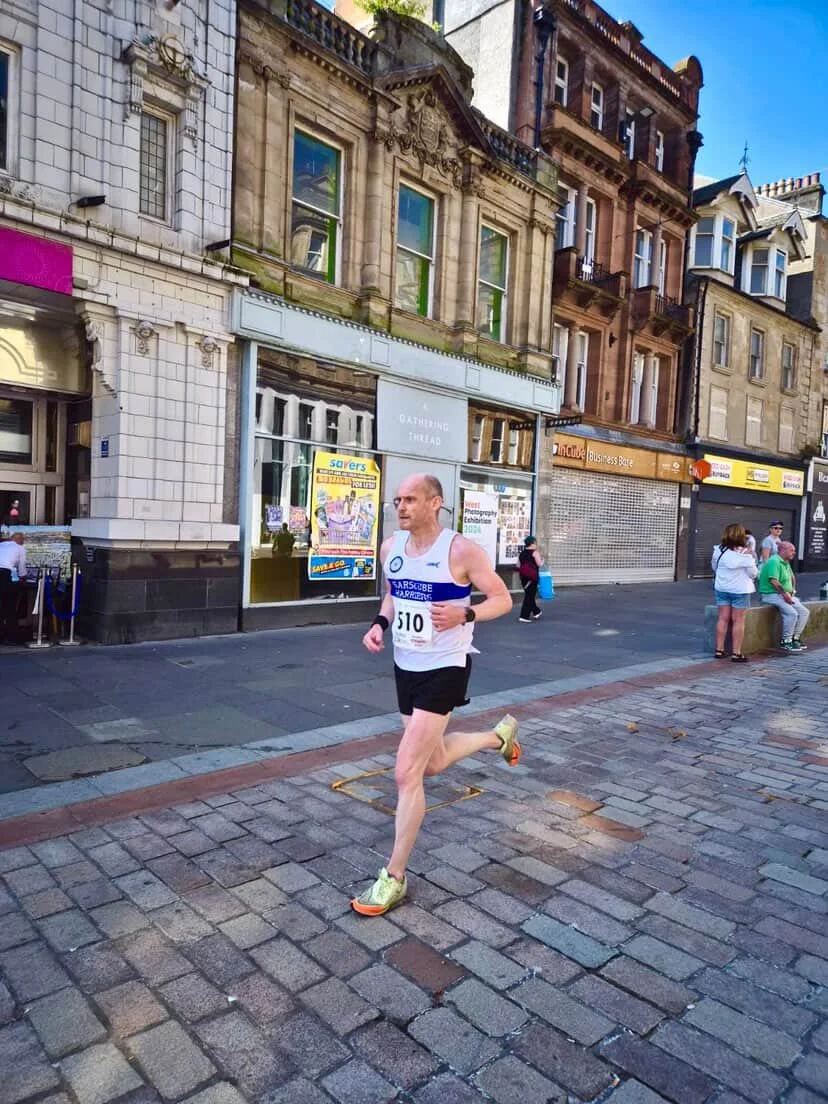 A man running in a race on cobblestone street in an urban area with historic buildings, some with ornate architecture, in the background.