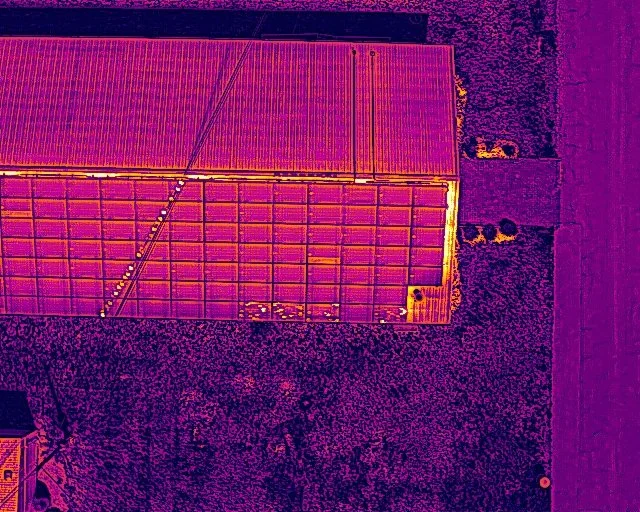 Aerial thermal image of a building with solar panels on the roof and surrounding land.
