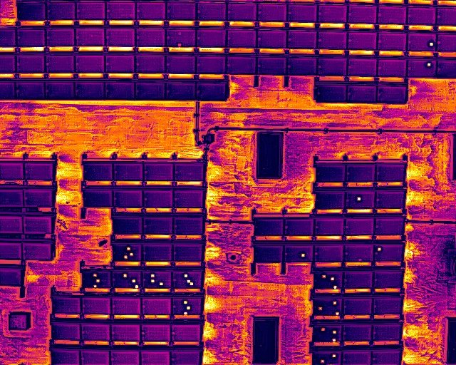 Infrared thermal image of a building facade showing different temperatures of bricks and windows, with warmer areas in yellow and cooler areas in purple.