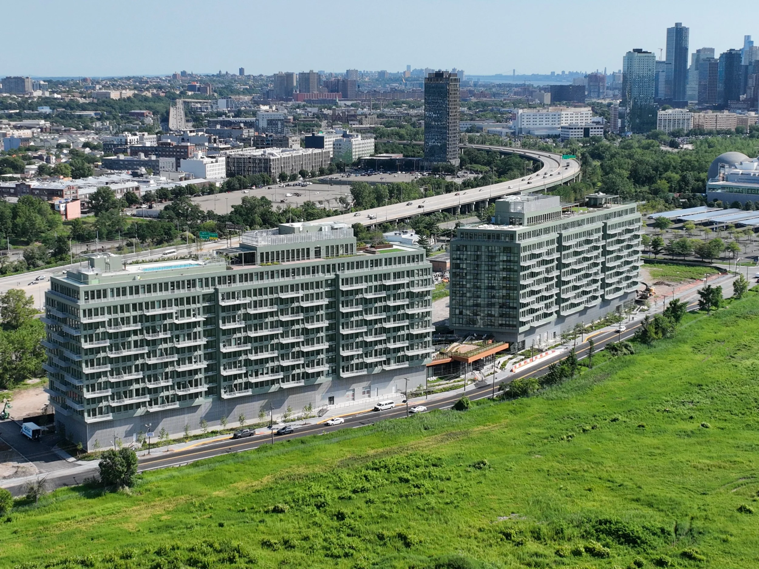 A city skyline with high-rise buildings, a highway, and green landscape in the foreground on a clear day.