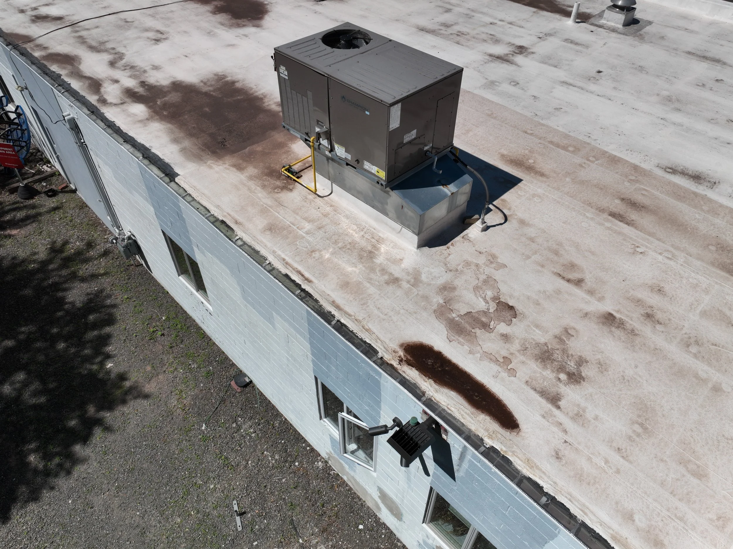 A rooftop with an HVAC unit, a vent, and weathered patches on the roofing surface.