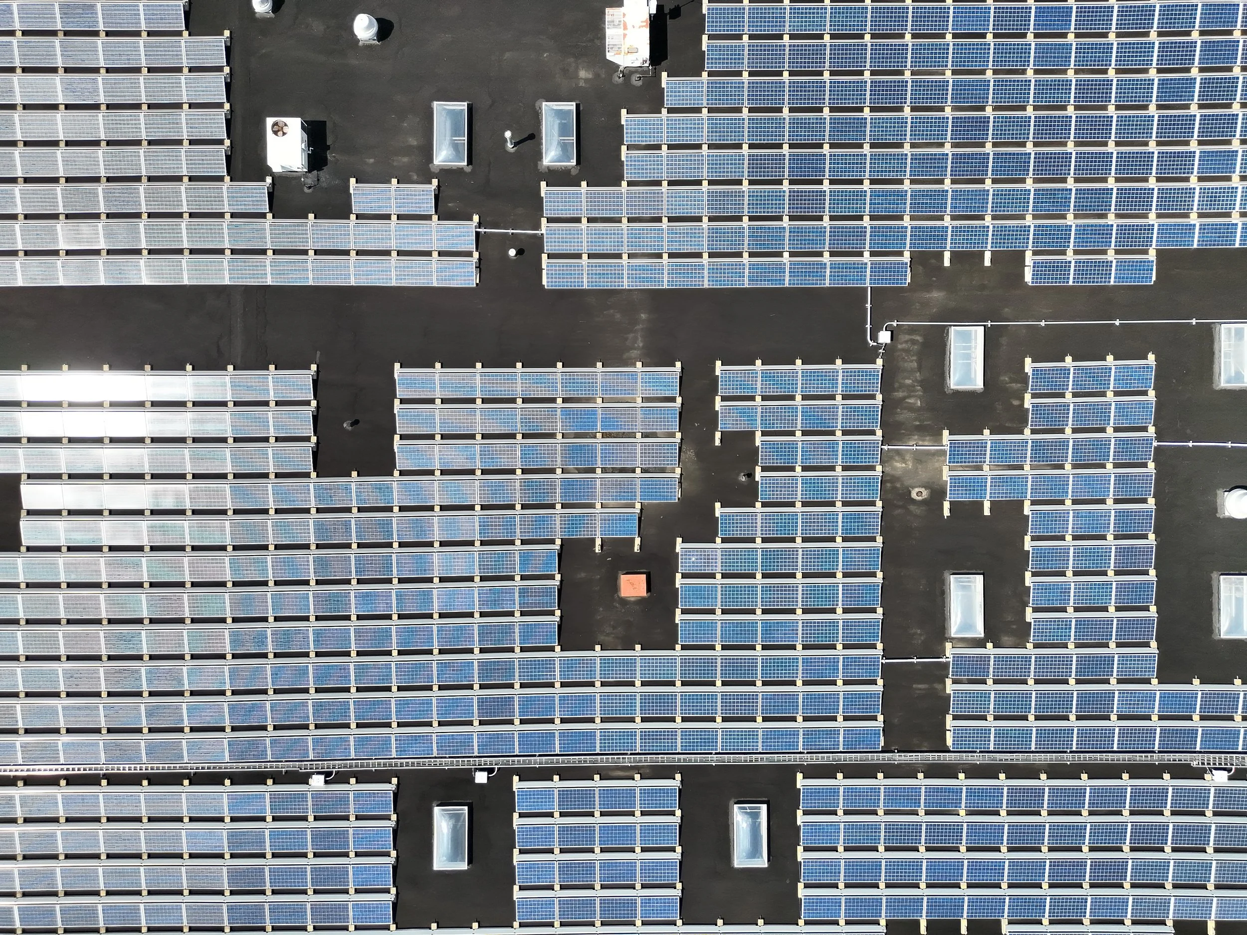 Aerial view of a large parking lot filled with solar panel arrays installed on the rooftops, with some HVAC units and vents visible among the solar panels.