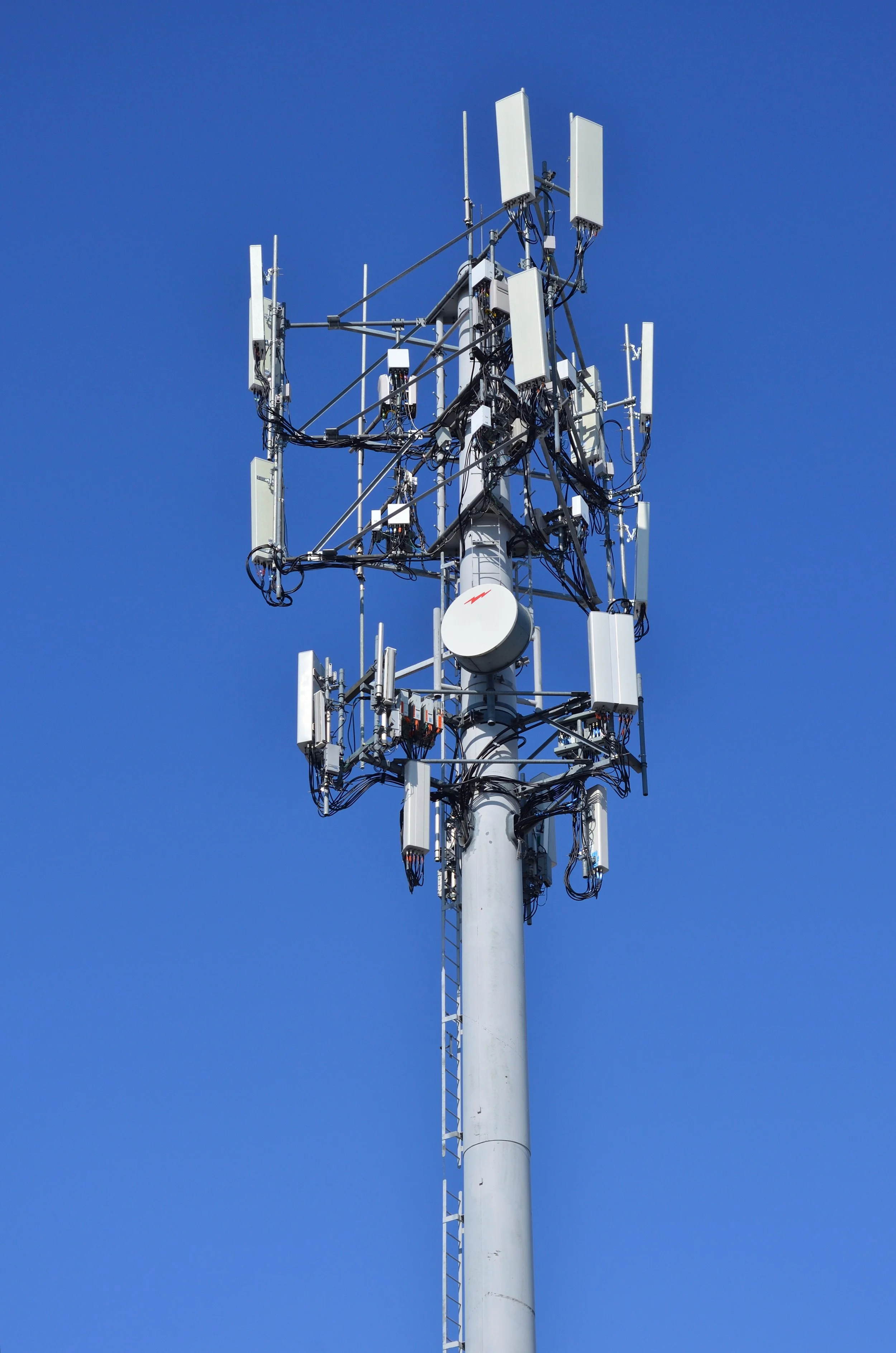 A tall cell tower with multiple antennas and cables against a clear blue sky.