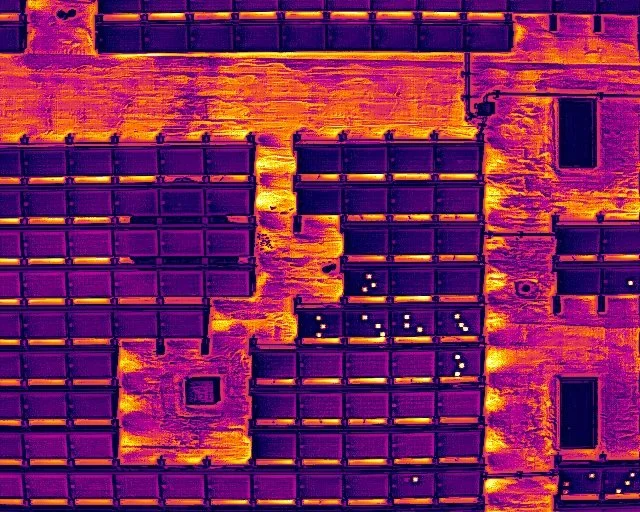 Infrared thermal image of a building facade with multiple windows, showing heat patterns in purple, orange, and yellow.