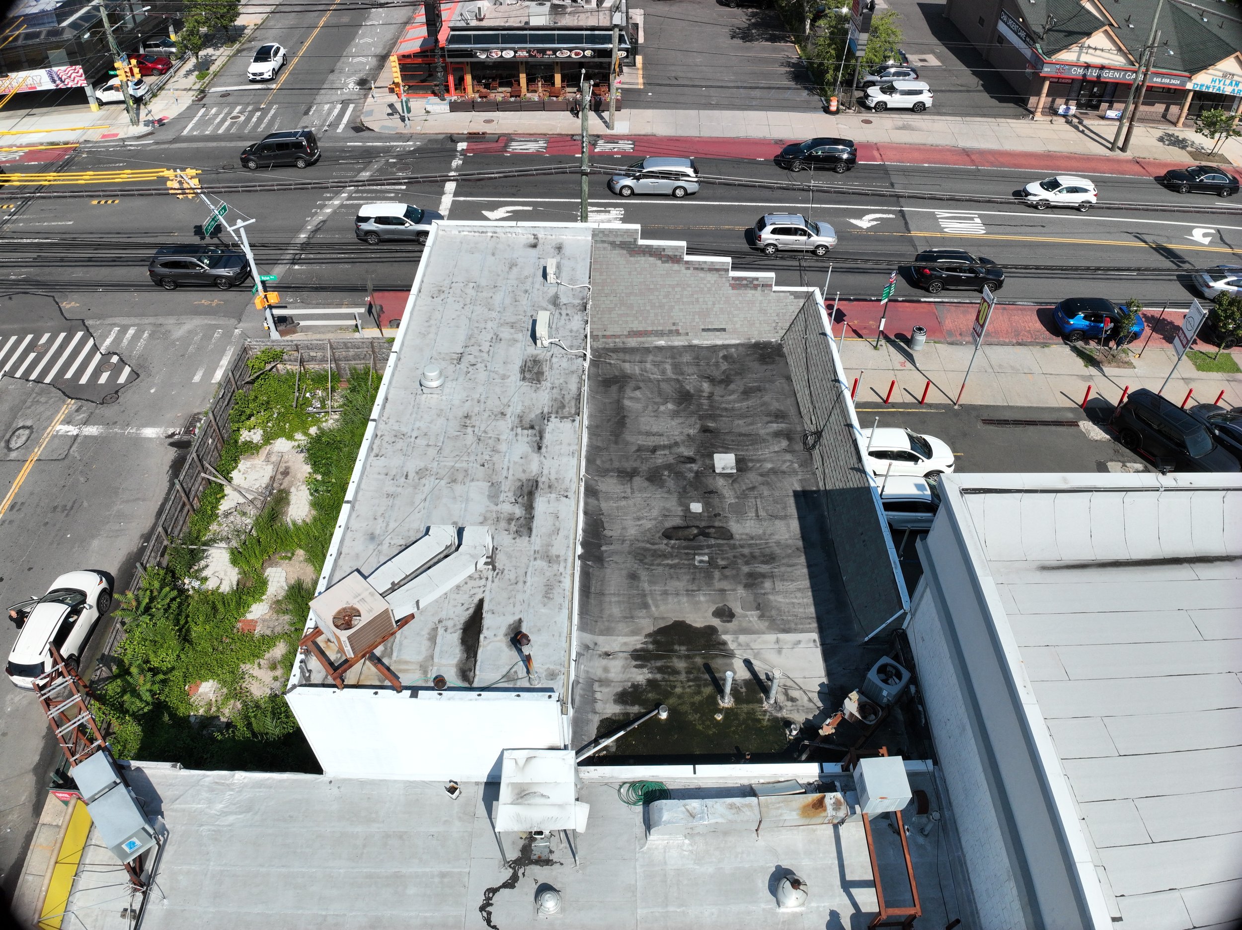 Aerial view of a city street intersection with cars, a red sidewalk, utility poles, and commercial buildings including a restaurant and dental office.