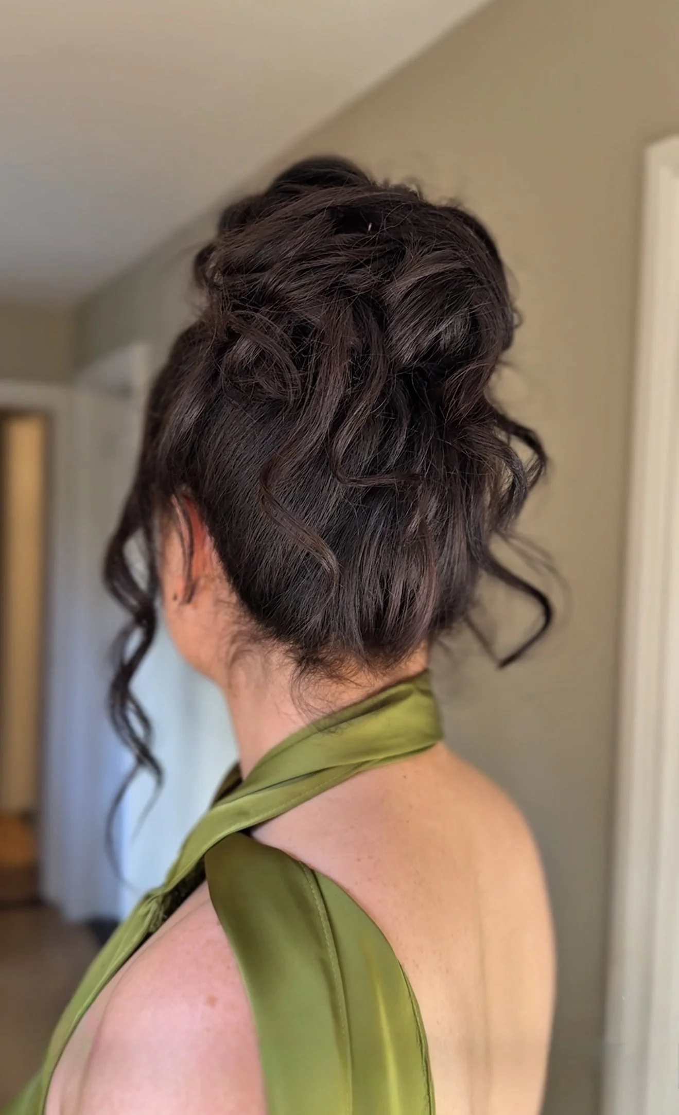 Back of a woman's head with an elegant updo hairstyle featuring curled strands and an olive green satin dress.
