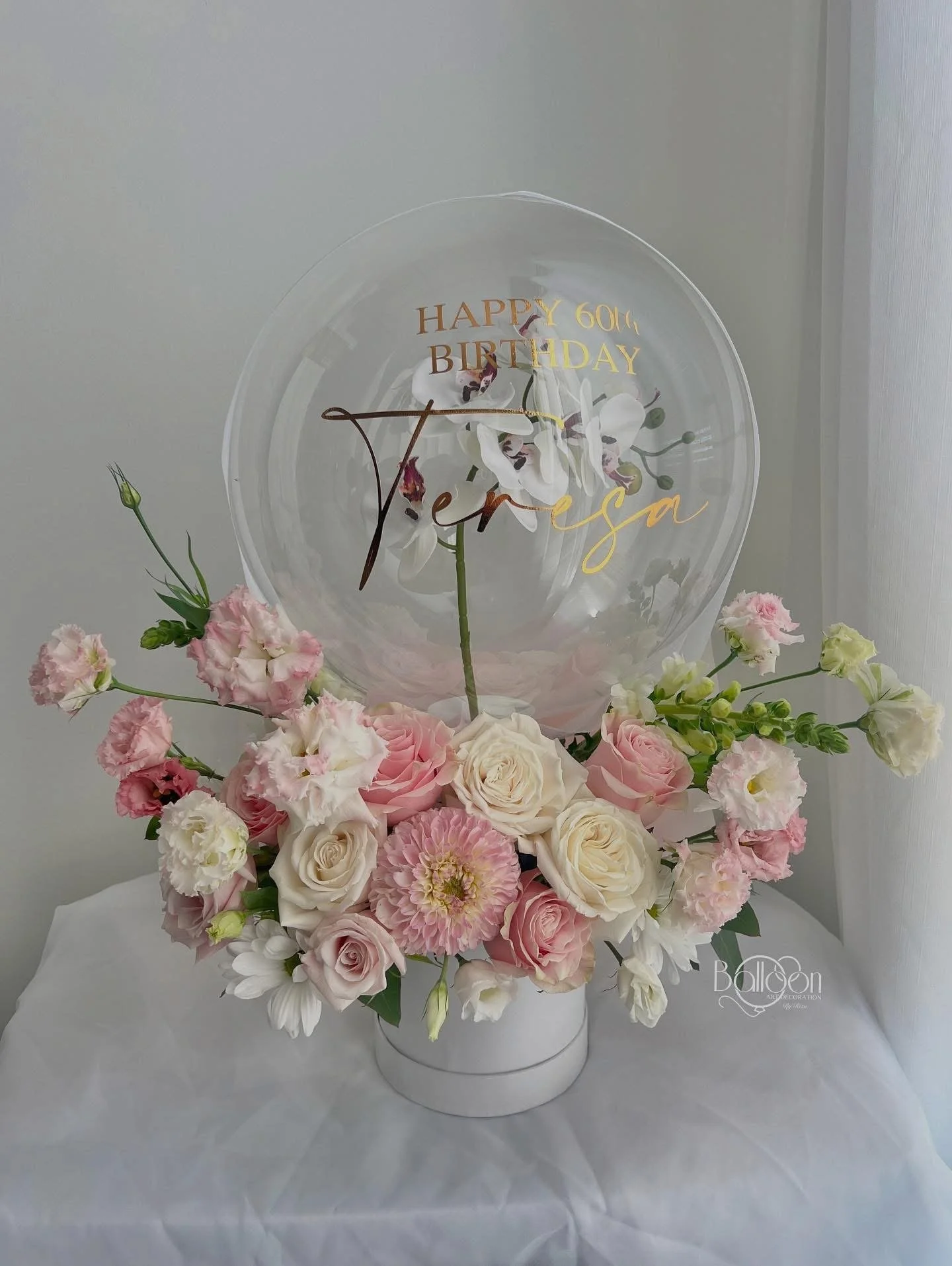 Flower arrangement with pink and white roses, pink dahlias, with a clear balloon that has a birthday message, and small white flowers in a white vase.