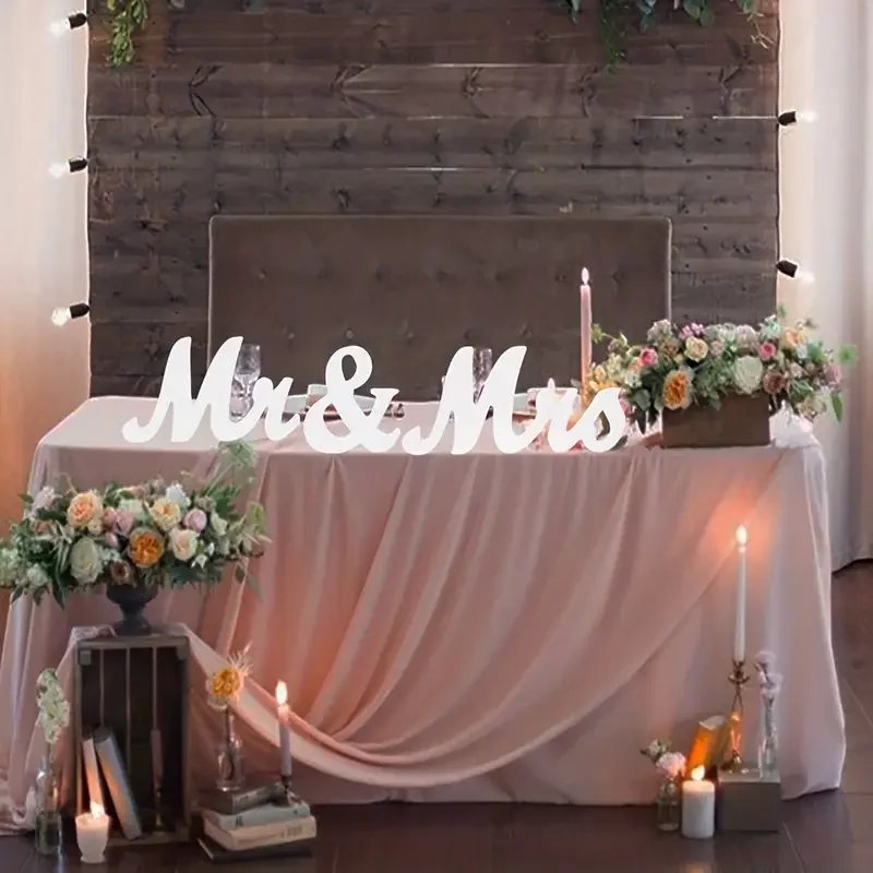 Wedding reception table decorated with pink drapery, floral arrangements, candles, and a white "Mr & Mrs" sign on a wooden backdrop.