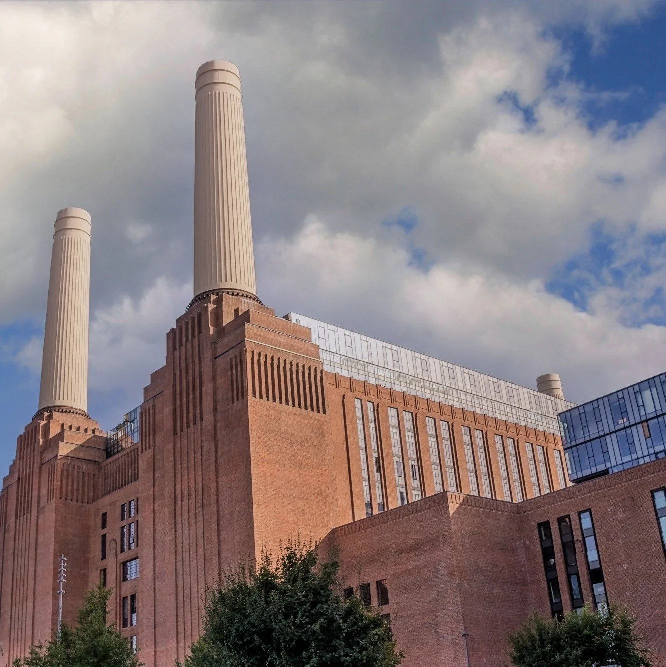 A large, historic power plant with brick walls and three tall smokestacks under a partly cloudy sky.