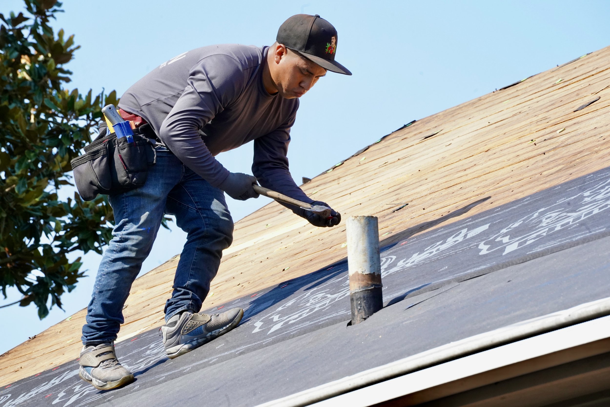 Man installing roof shingles using hammer on house roof.