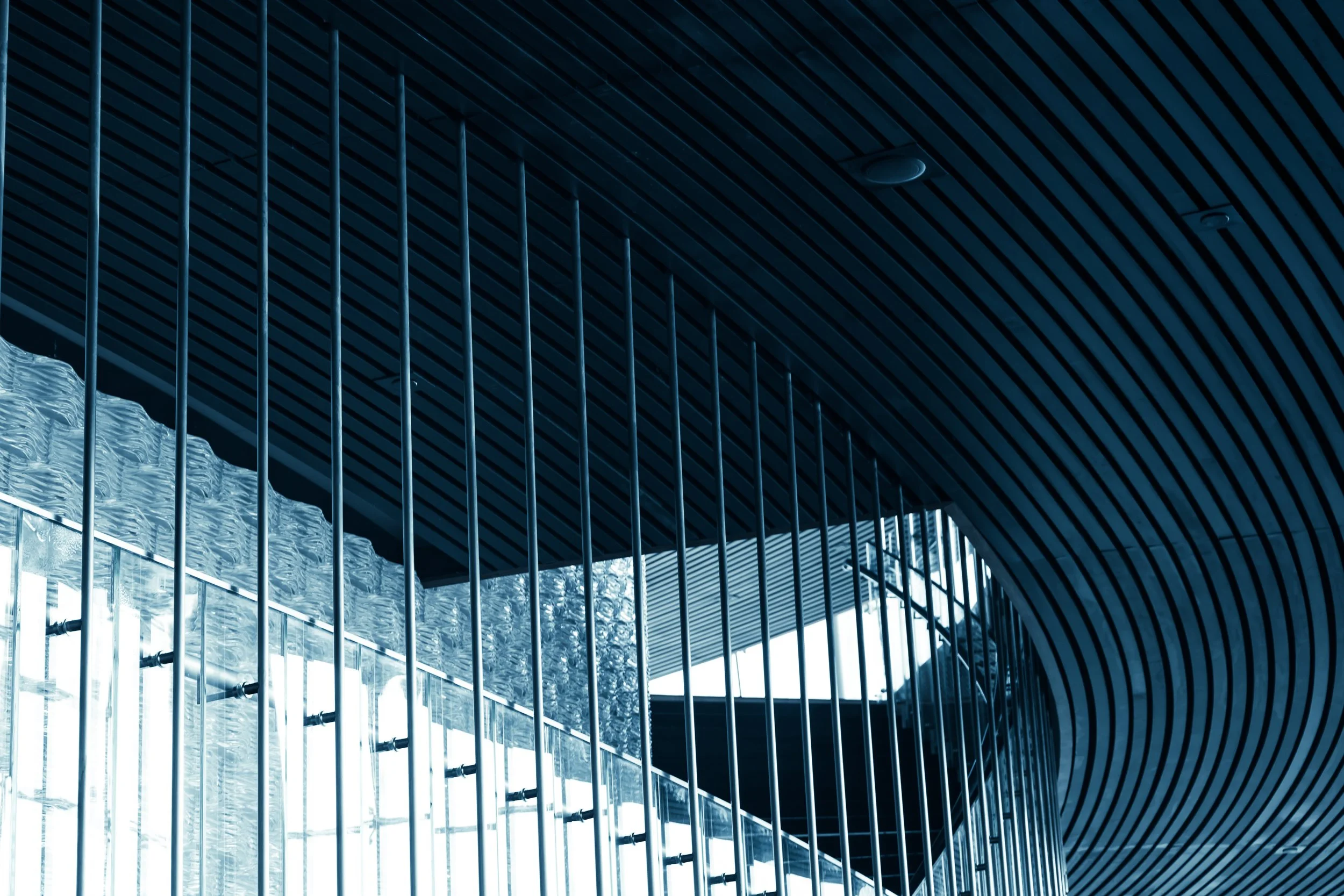 Interior view of a modern building with curved ceiling and vertical metal railings, with natural light from windows.