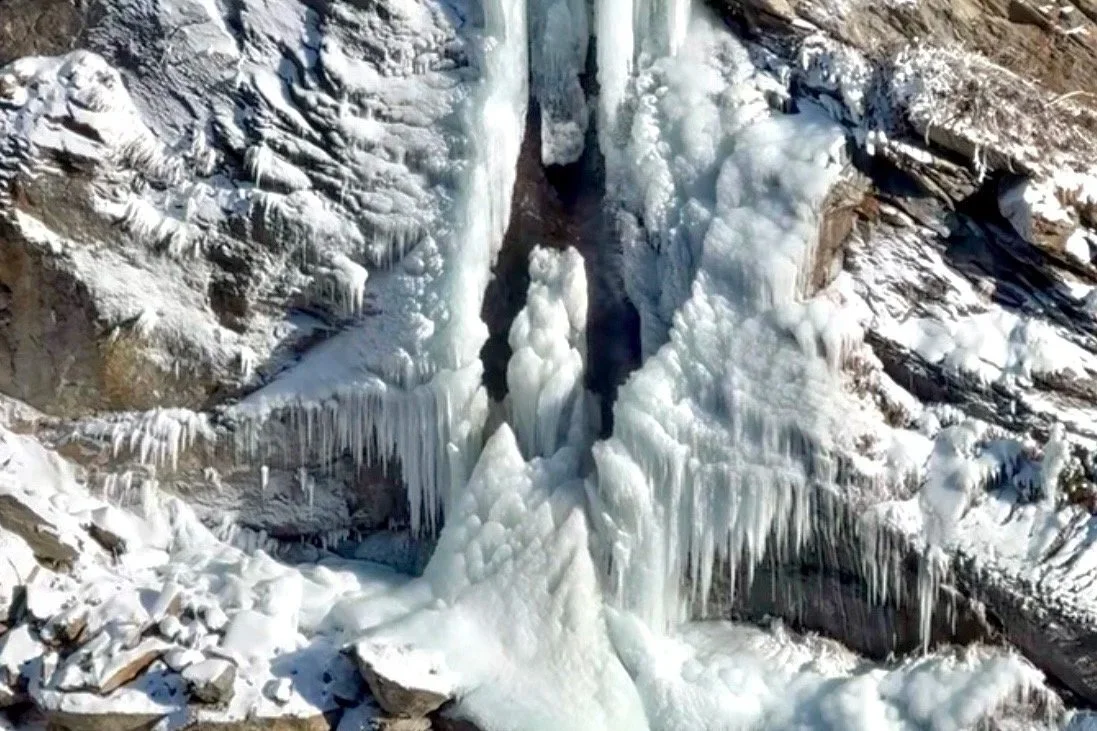 Cascata ghiacciata e ghiaccio su una parete rocciosa in un ambiente invernale.