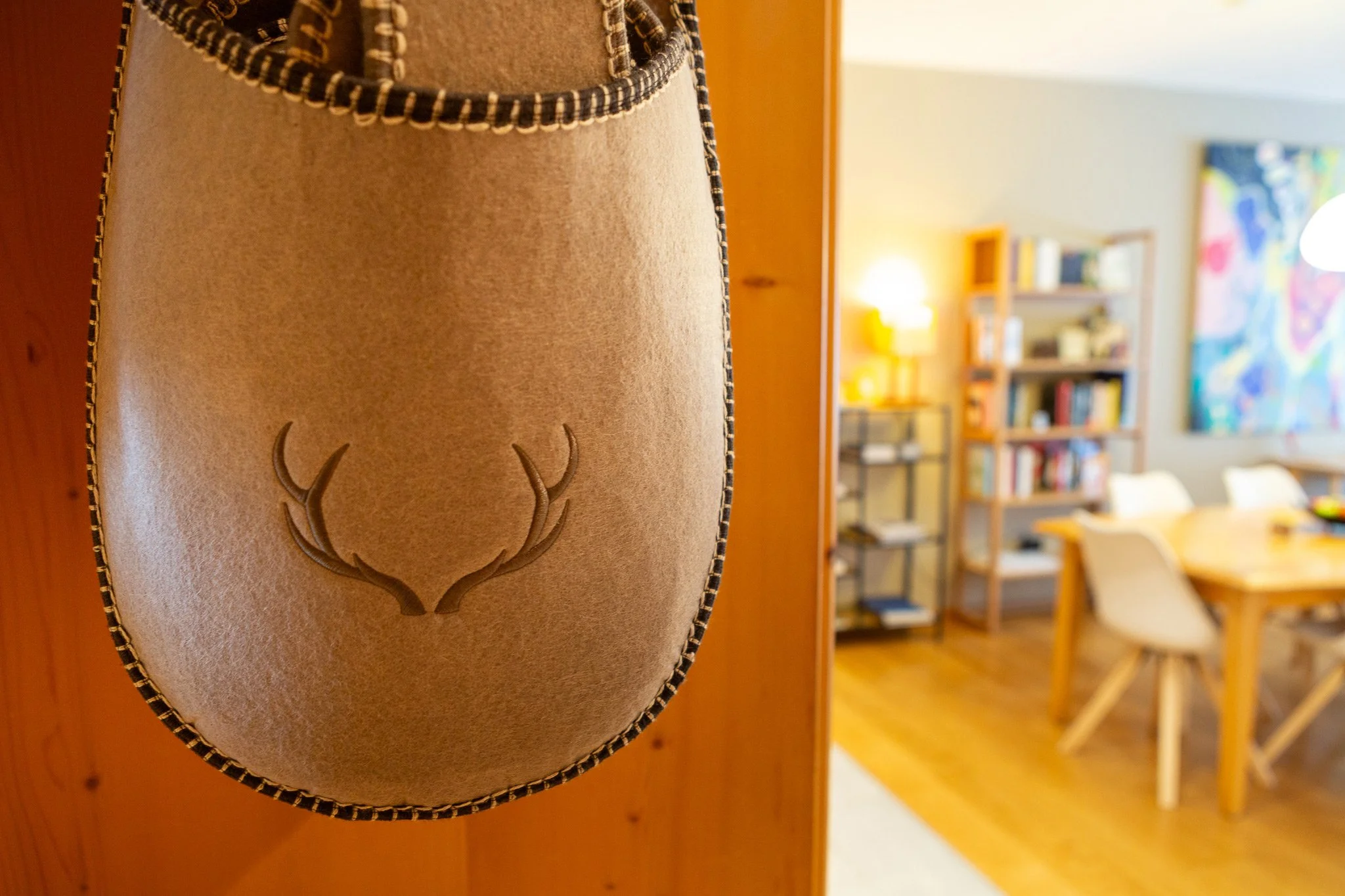 Porta pantofole con disegno di corno di cervo appesa a una porta, con soggiorno con libreria e tavolo in legno in secondo piano