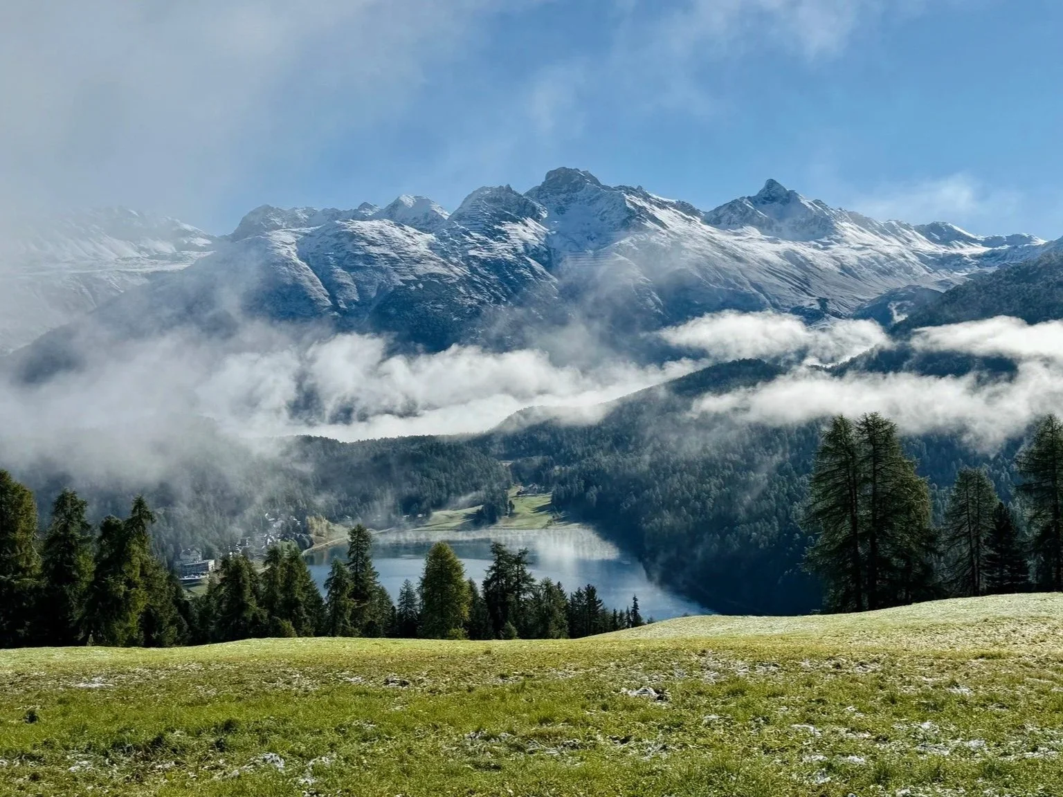 Paesaggio montano con neve, foresta di alberi e lago, nuvole sul cielo.