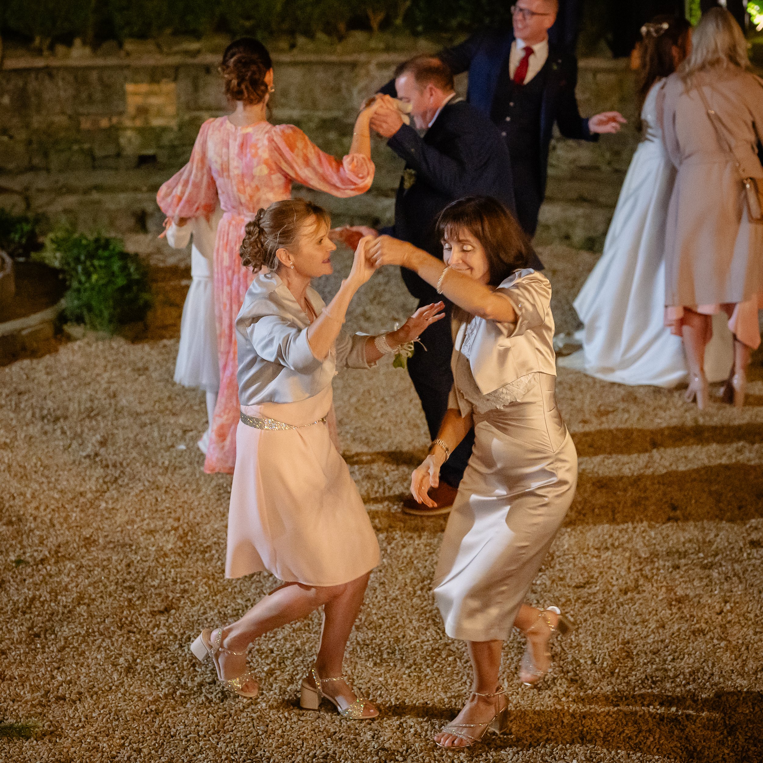 Two women dancing at a social gathering with others dancing in the background.