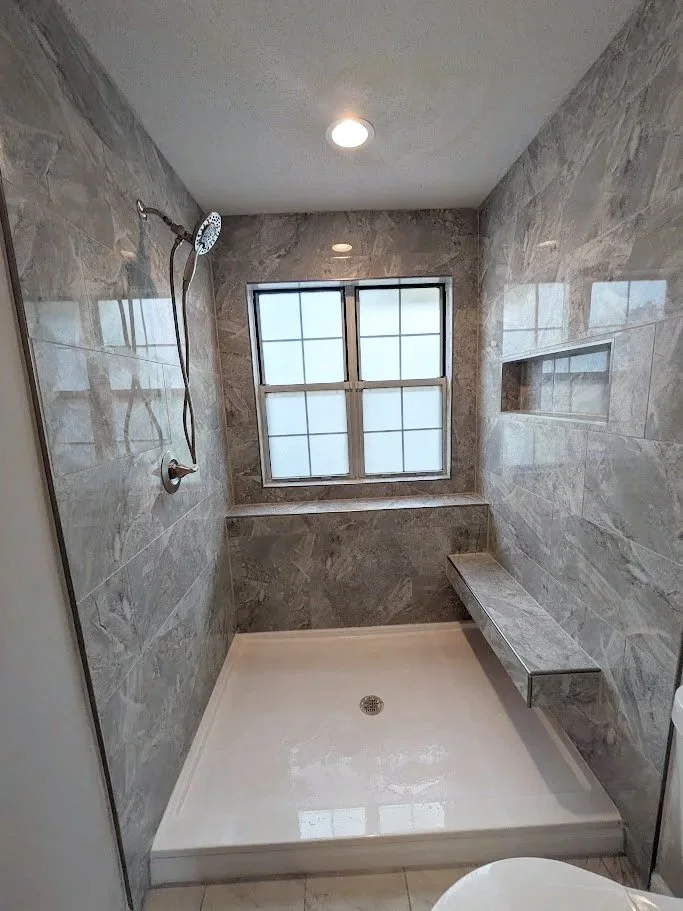 Modern walk-in shower with gray marble walls, a built-in bench, frosted glass window, and a rain shower head.