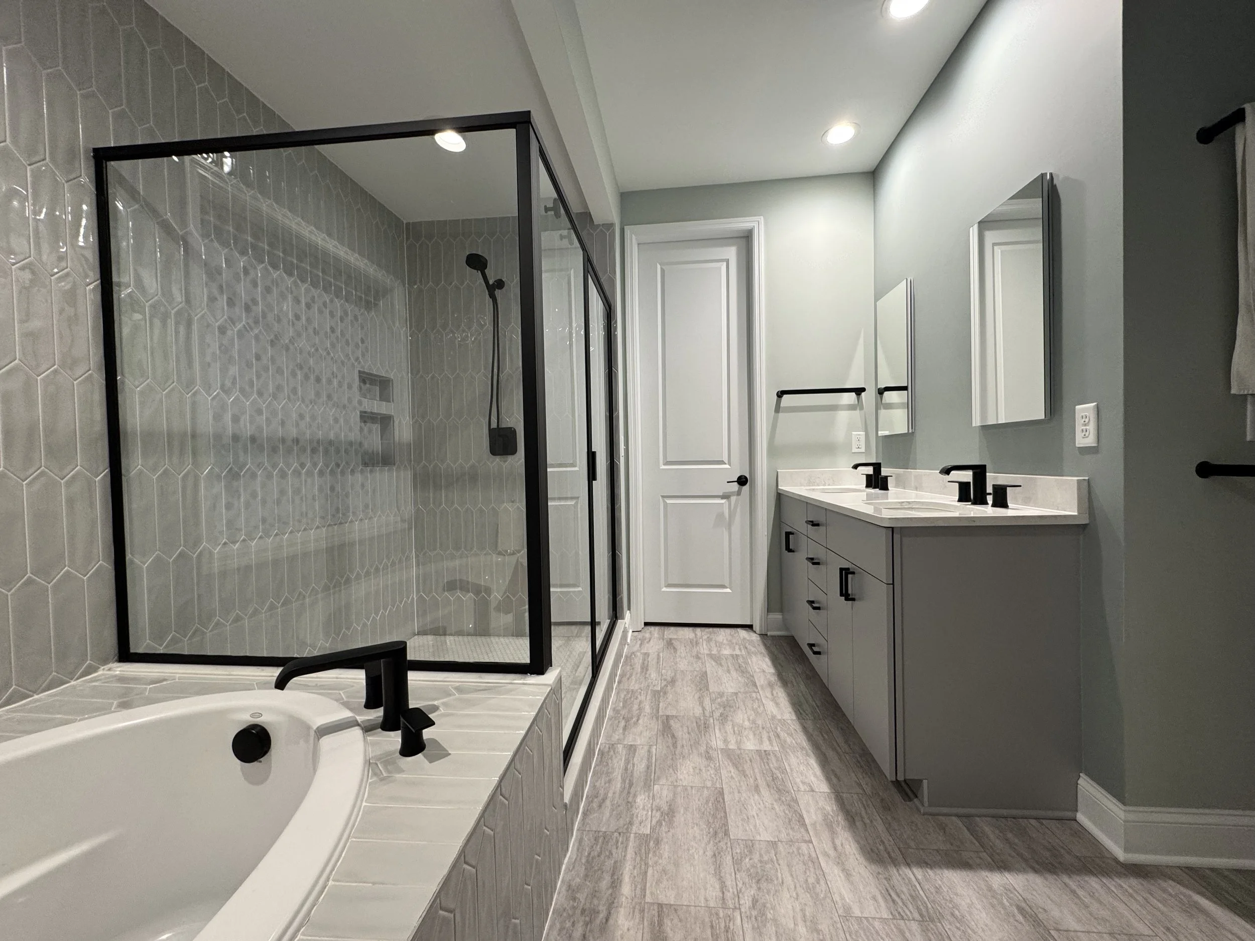 Modern bathroom with glass-enclosed shower, gray tile walls, vanity with double sinks, and gray wood-look flooring.