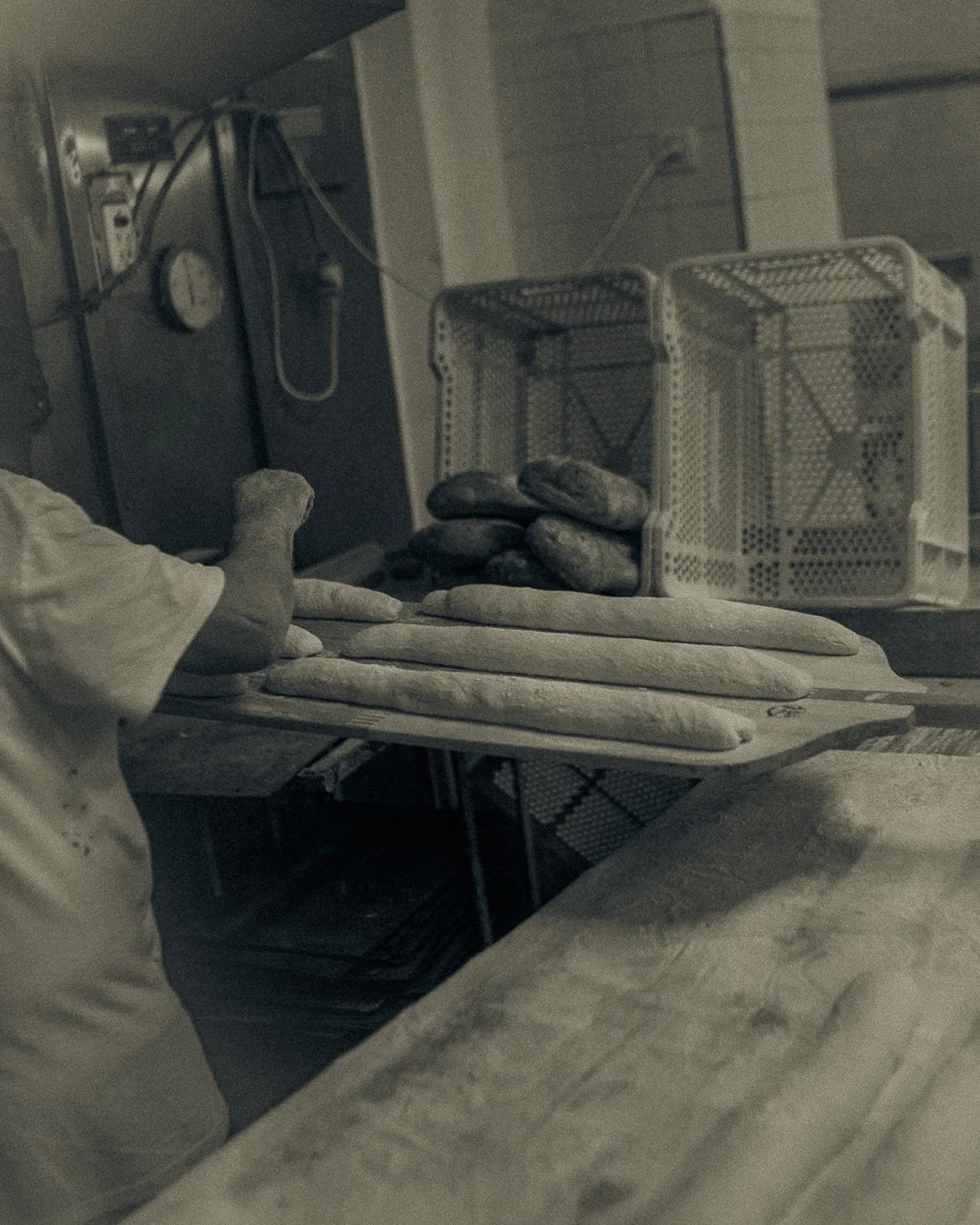 Baker's hands holding a wooden tray with raw bread loaves ready for the oven at Horno El Reloj, El Cabanyal, Valencia