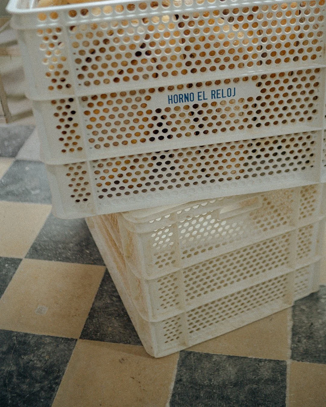 Stacked bread baskets stamped with Horno El Reloj on the checkered floor of the traditional bakery in El Cabanyal, Valencia