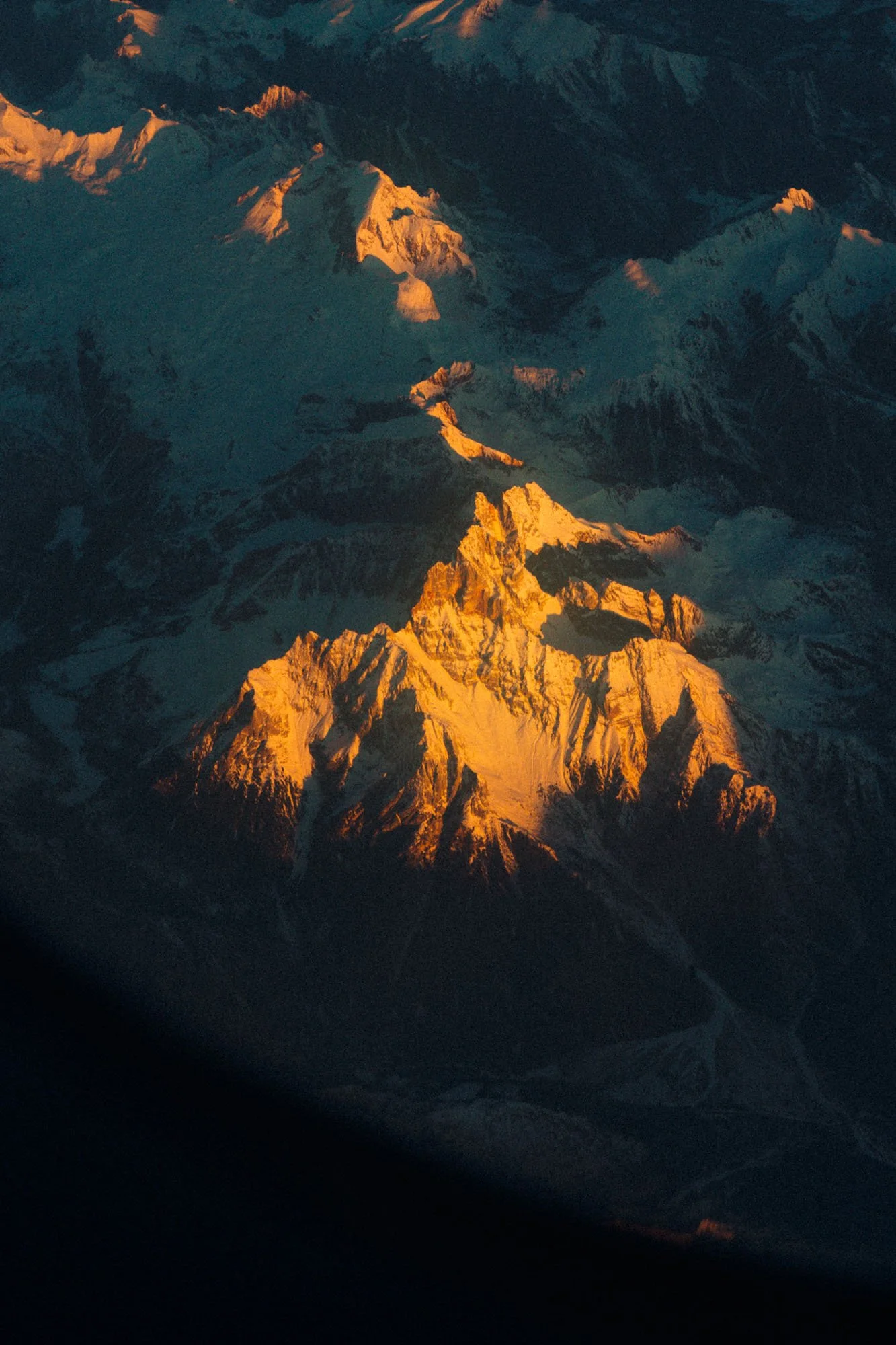 Montañas nevadas al atardecer con tonos dorados y oscuros en la sombra.