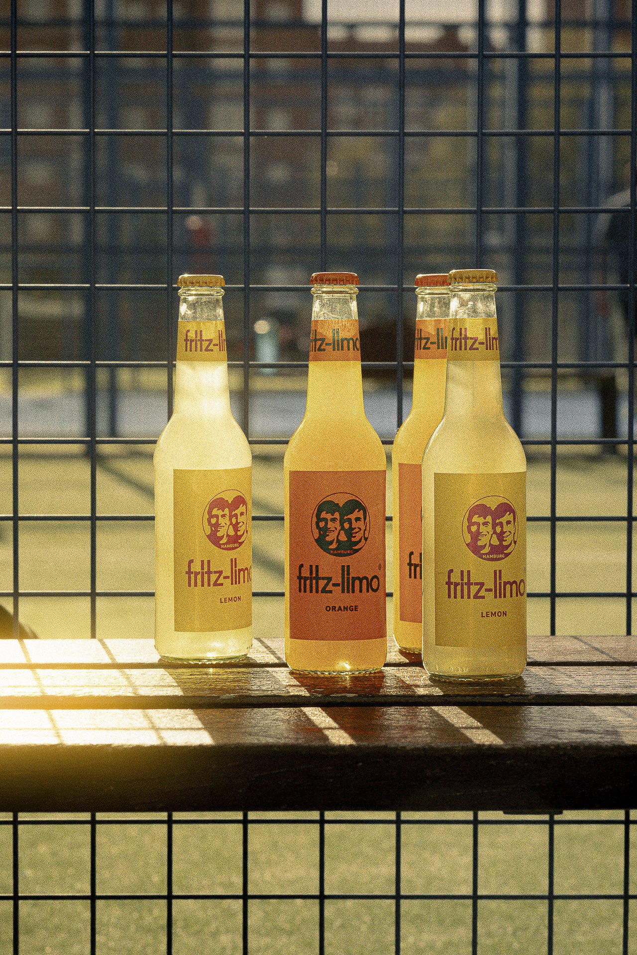 Three glass bottles on a sunlit fence, premium beverage styling for boutique hotels and restaurant storytelling for Fritz-limo