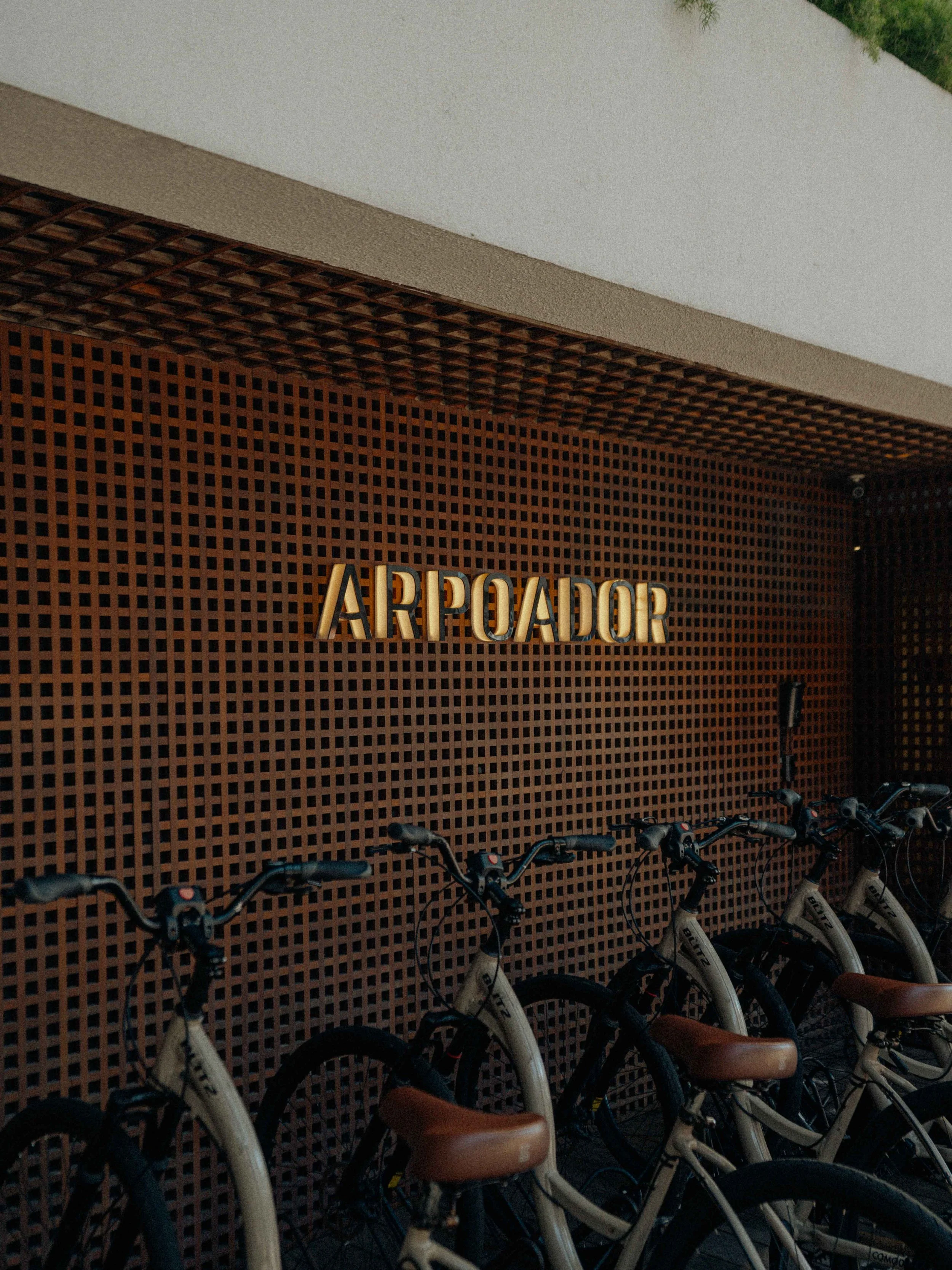 Estación de bicicletas llamada 'ARROADOR' con varias bicicletas estacionadas frente a un muro de rejilla marrón con un letrero metálico dorado que dice 'ARROADOR'.