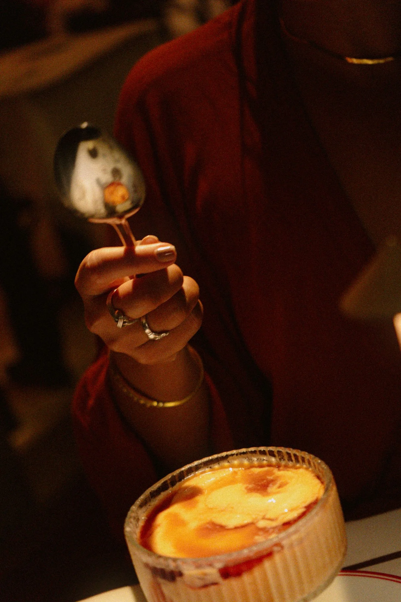 Persona sosteniendo una copa de cóctel con crema y caramelo, con comida en primer plano en un ambiente oscuro.