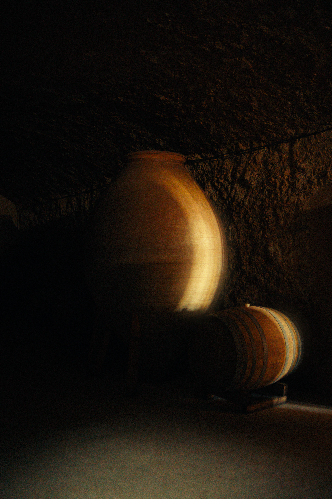 Large clay tinaja and oak barrel side by side in the underground cellar at Celler del Roure, Moixent — ancient and modern winemaking methods coexisting