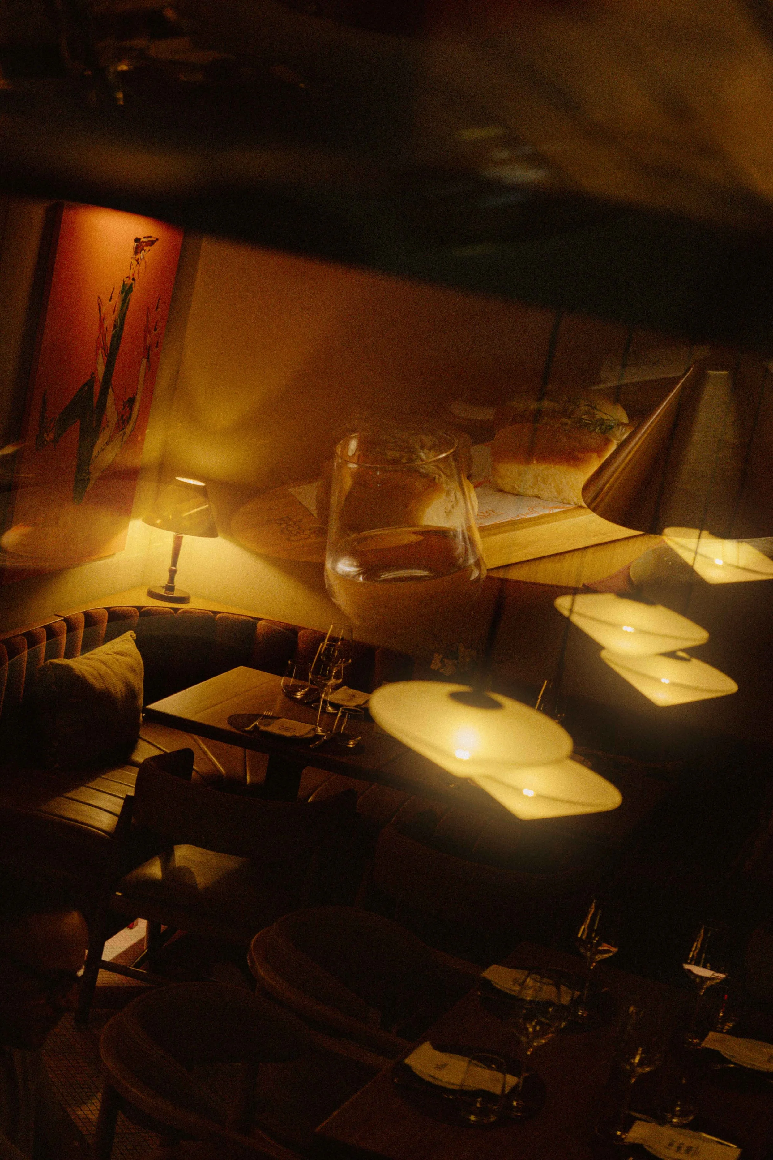 Una mesa con cristalería y utensilios de comida, en un ambiente con iluminación cálida, decoraciones de lámparas y arte en la pared.