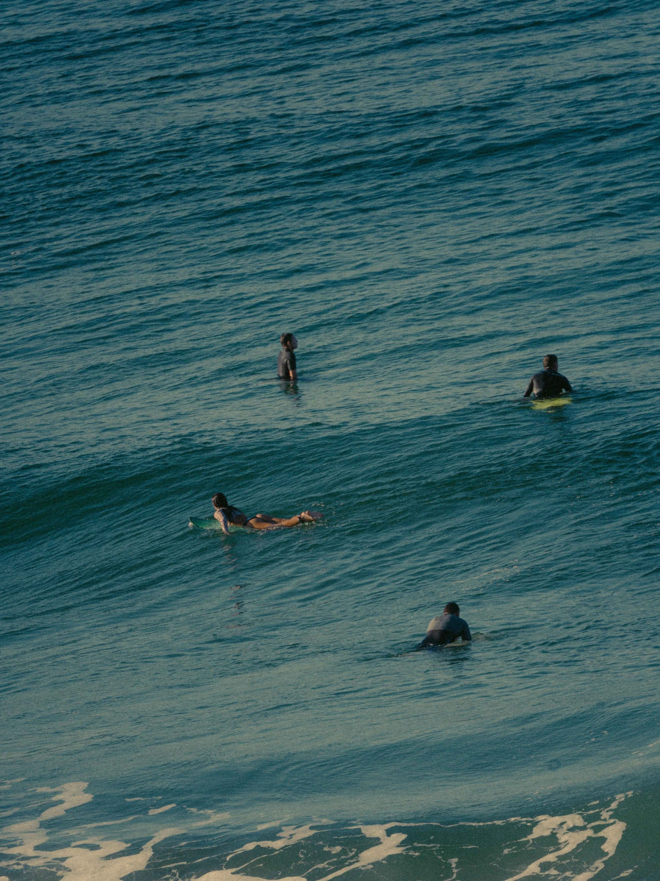 Personas en el mar, algunas caminando por el agua y otra más acostada en una tabla de surf.