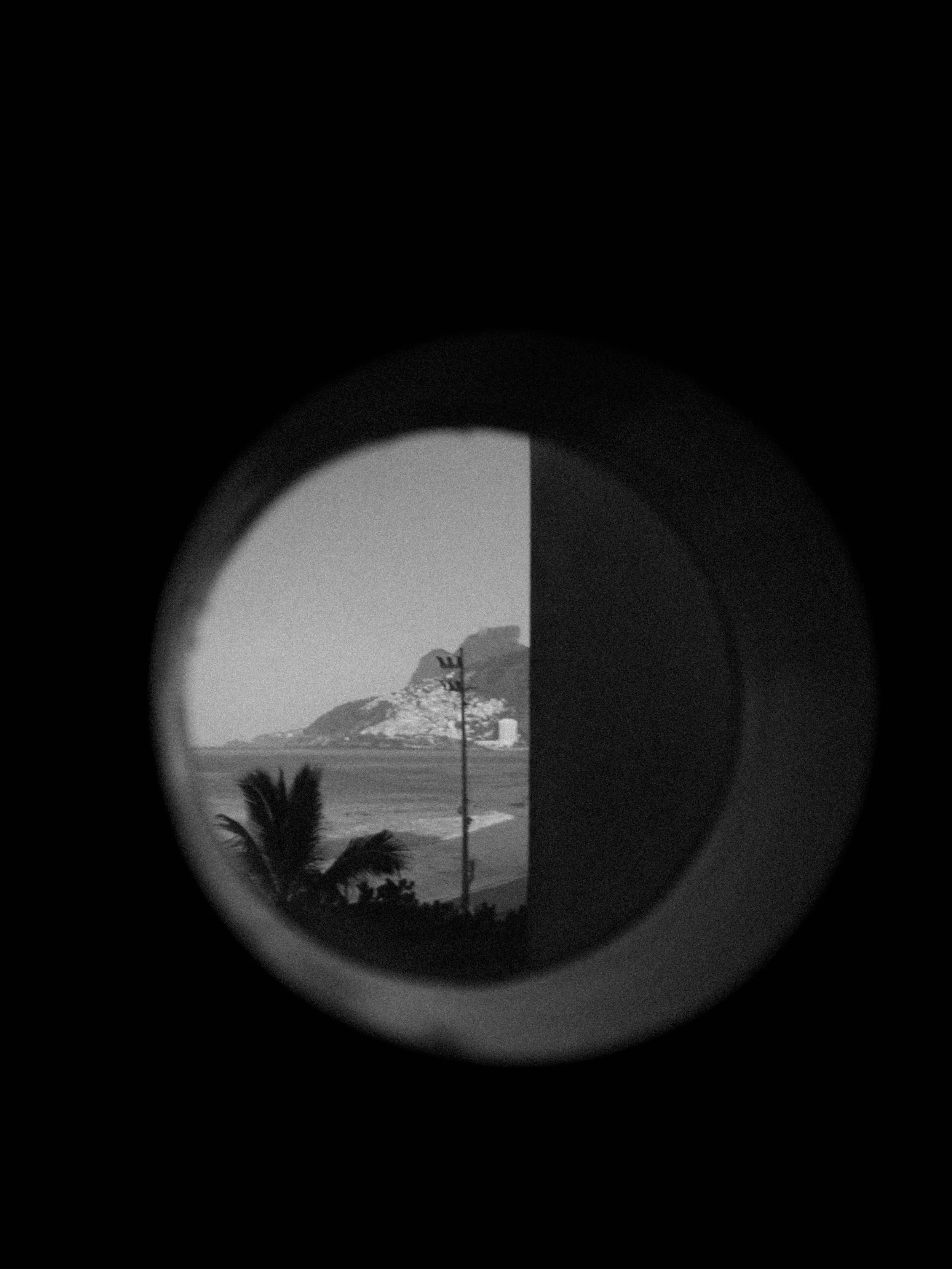 Vista en blanco y negro a través de un objetivo o lente circular que muestra palmeras, colinas y una estructura en el paisaje