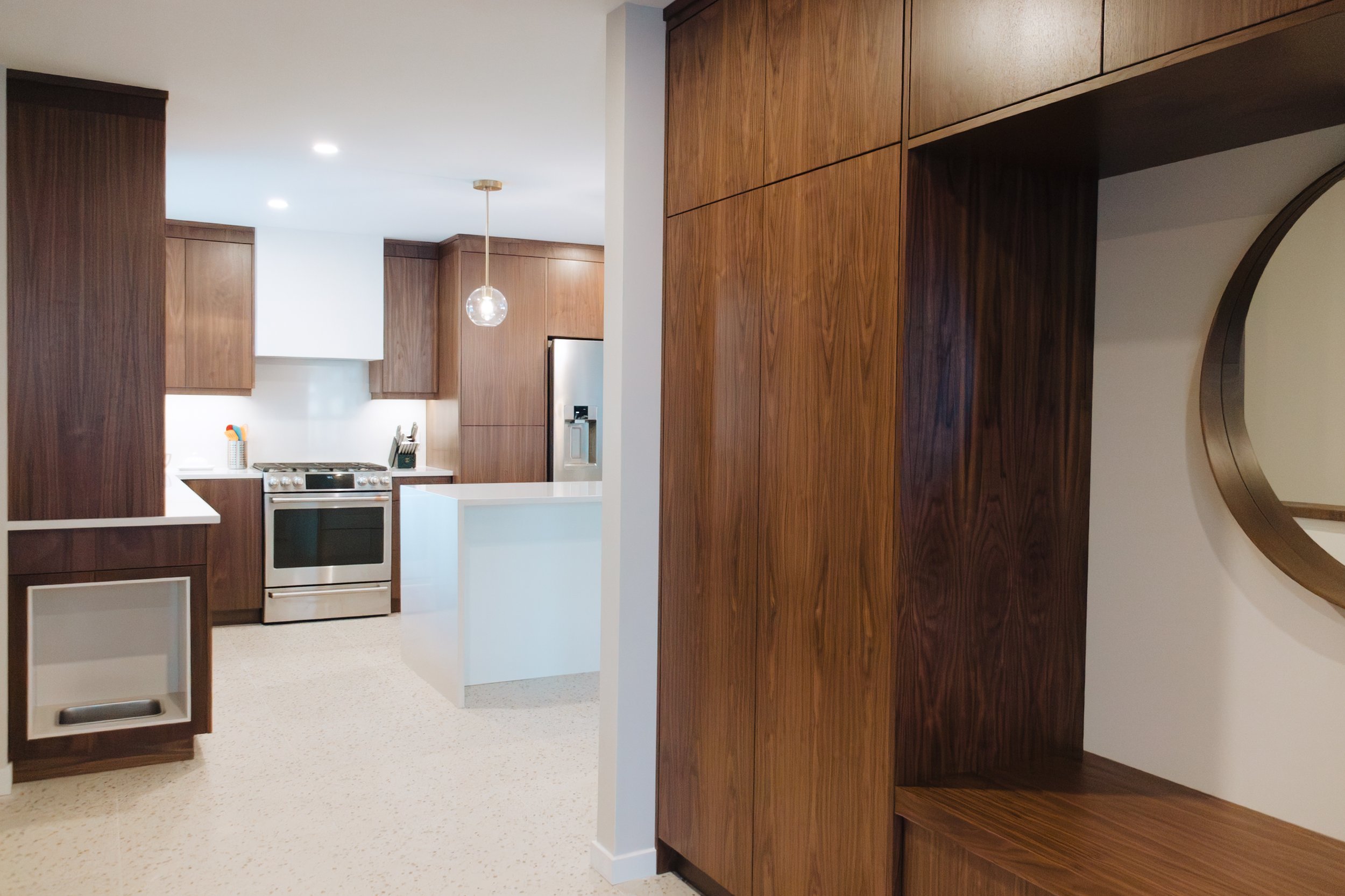 Modern kitchen with white countertops, wooden cabinets, stainless steel appliances, and a hanging globe light.