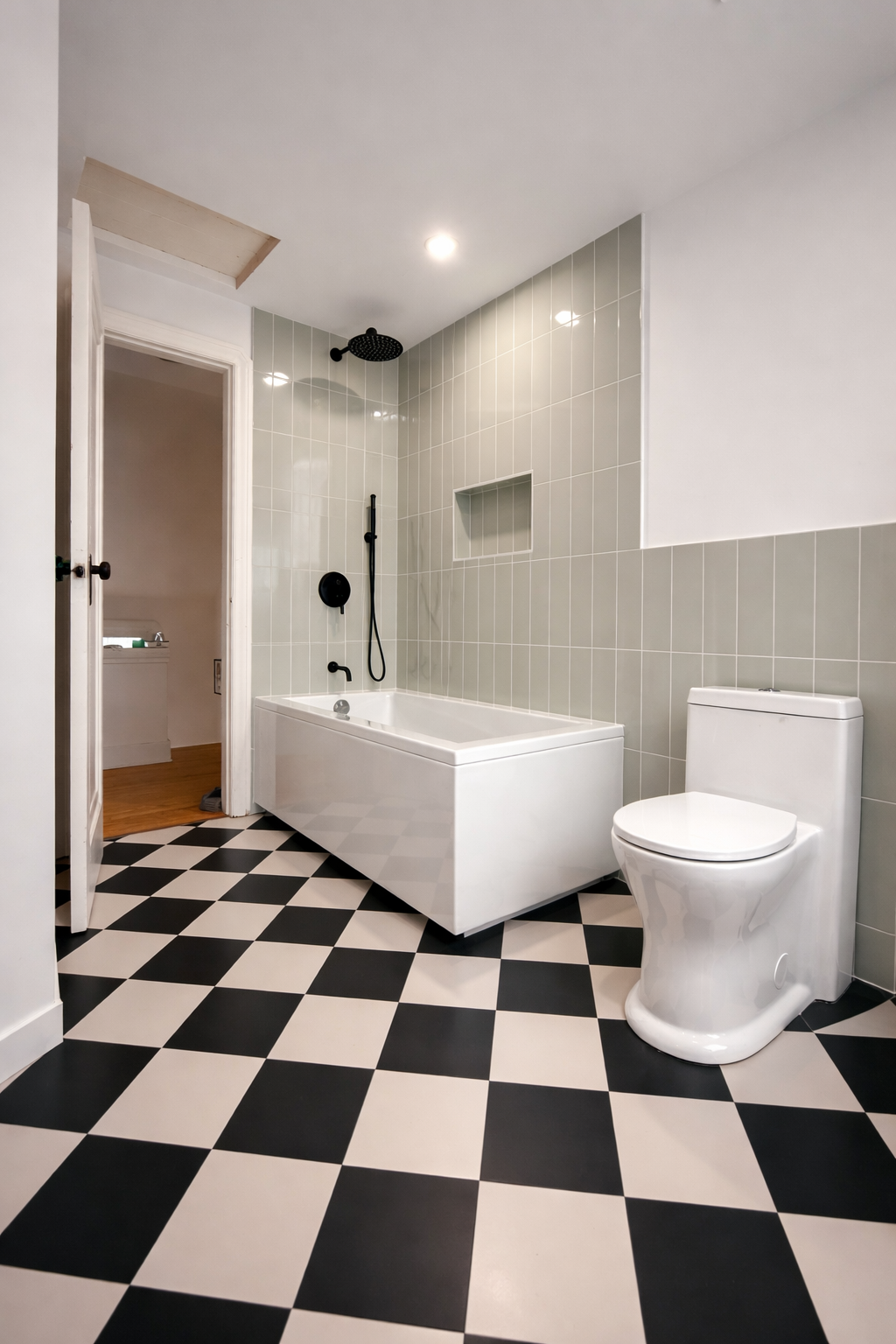 Modern bathroom with black and white checkered floor, white bathtub with black fixtures, black showerhead, and gray tiled wall, with a white toilet