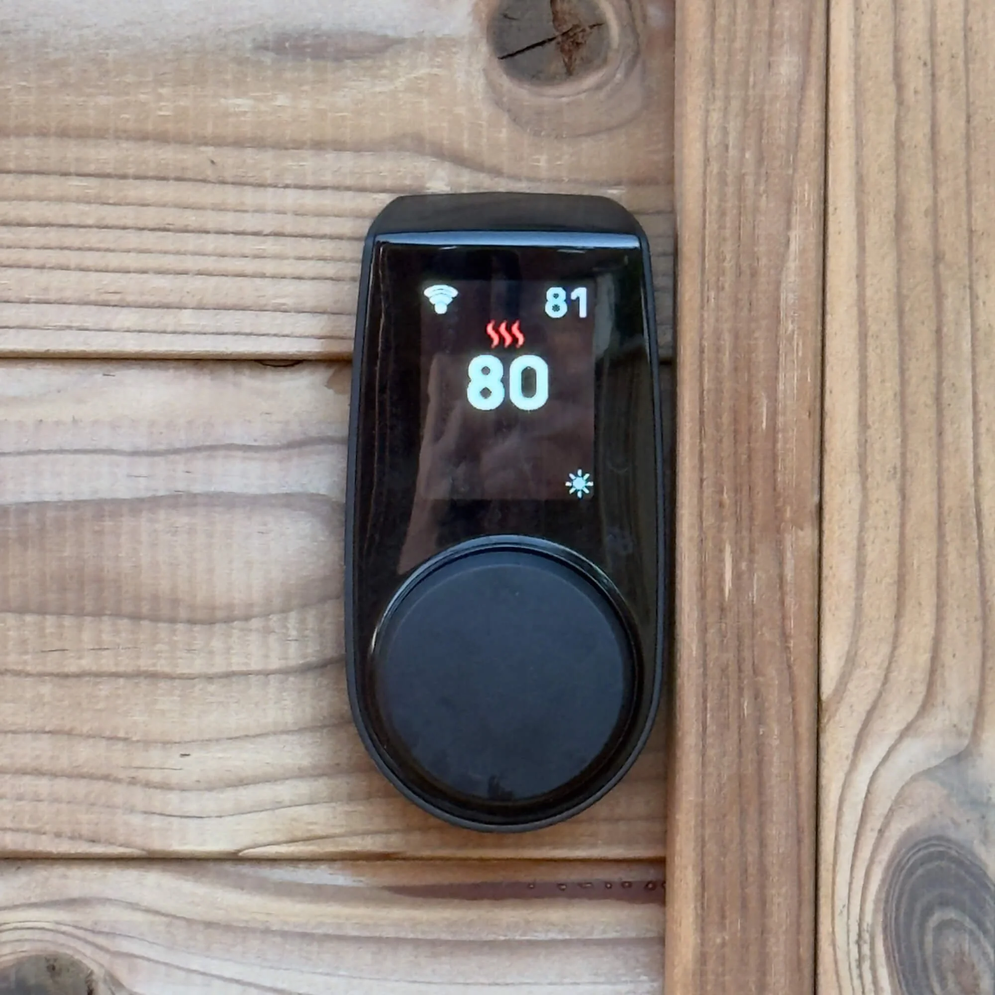 Digital thermostat mounted on wooden wall, showing temperature of 80 degrees with Wi-Fi signal and a small snowflake icon.