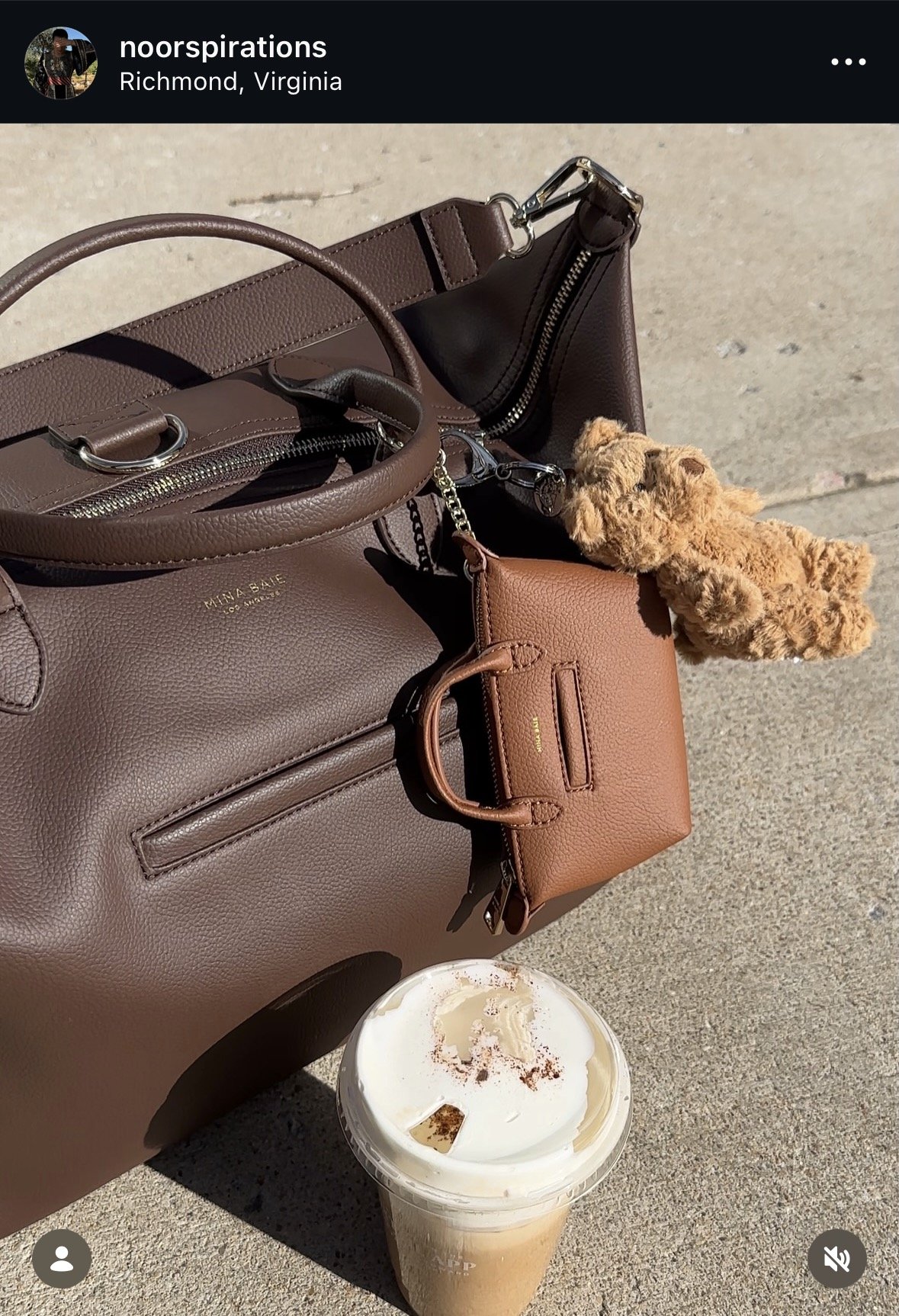 A collection of handbags and a small plush teddy bear on a concrete surface with a cold brew coffee drink in the foreground.