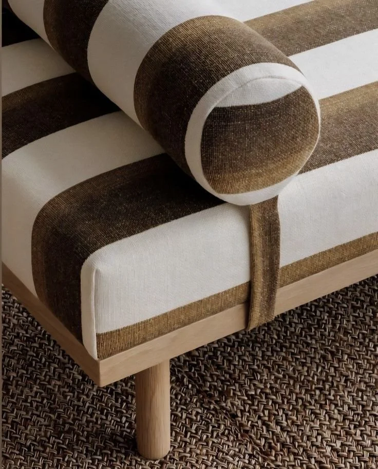 A sofa with brown and white striped upholstery and a matching round bolster pillow, placed on a woven carpet.