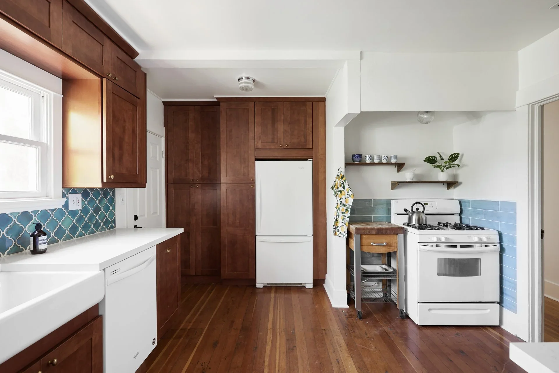 Kitchen with white appliances, brown cabinetry, a tiled backsplash, and hardwood floors.